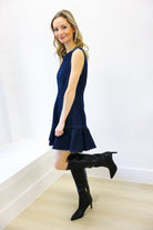 Woman wearing a navy dress and black knee-high boots against a white wall.