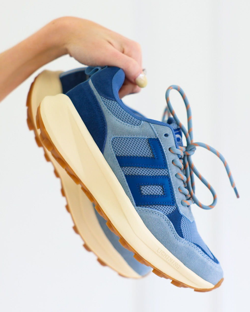 Blue Back70 sneakers with beige soles held by a person against a white background
