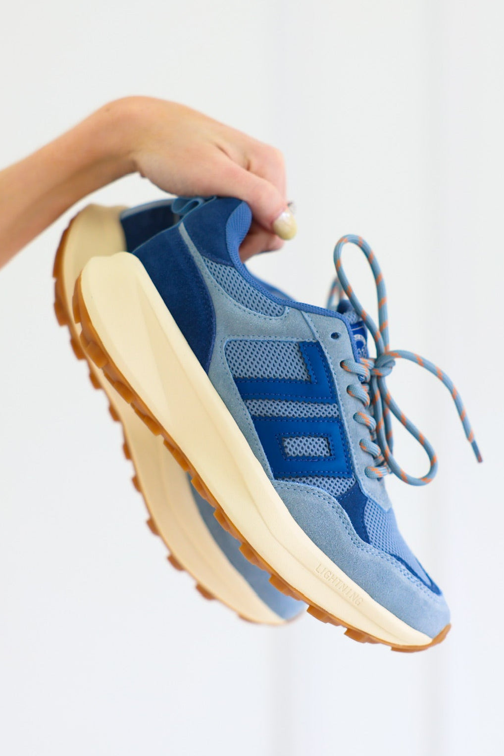 Blue Back70 sneakers with beige soles held by a person against a white background