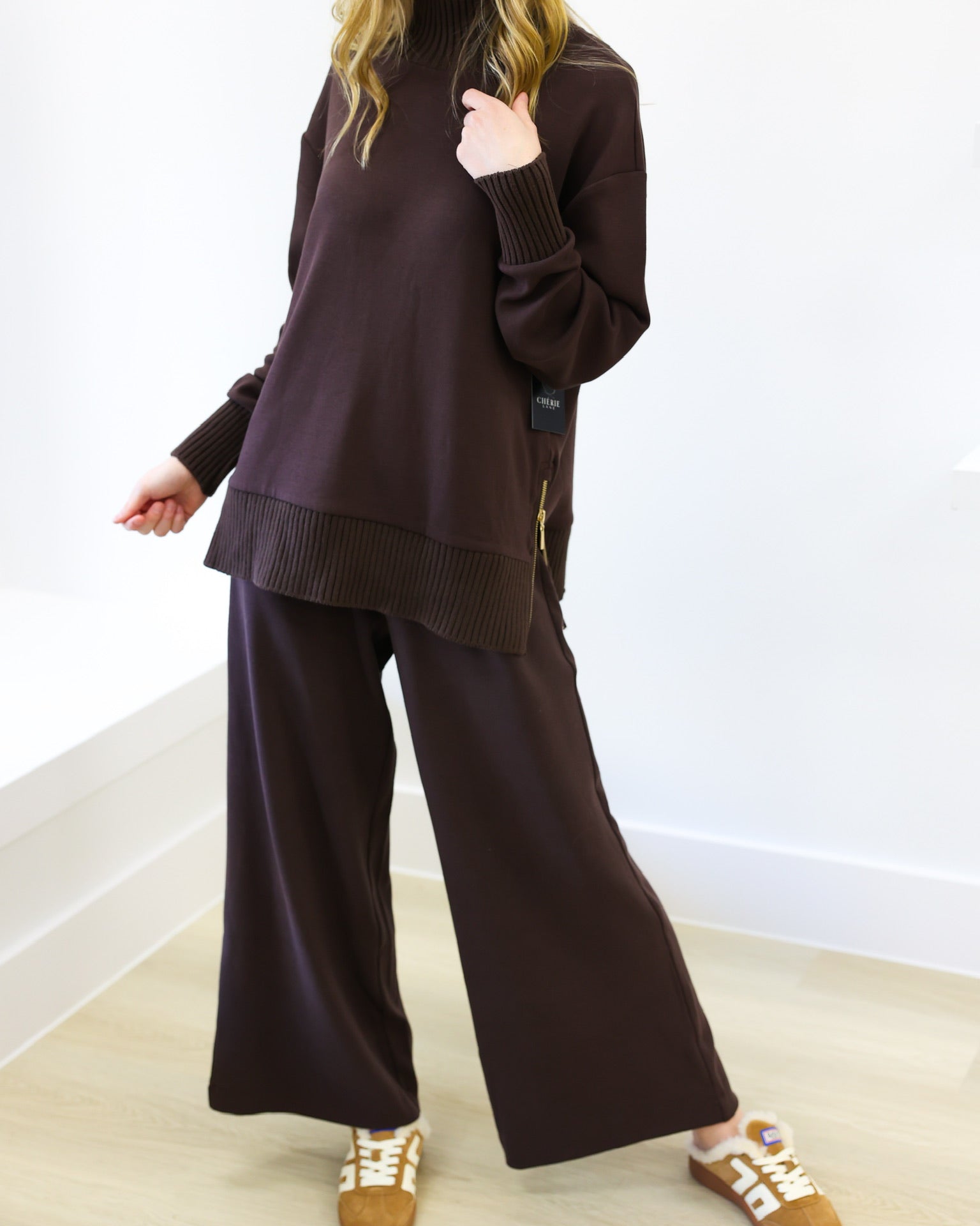 Woman wearing a brown outfit with wide-leg pants and a high-neck top on a white background