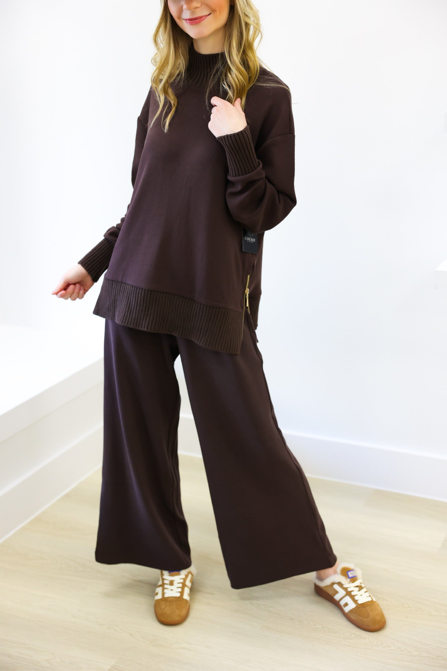 Woman wearing a brown outfit with wide-leg pants and a high-neck top on a white background