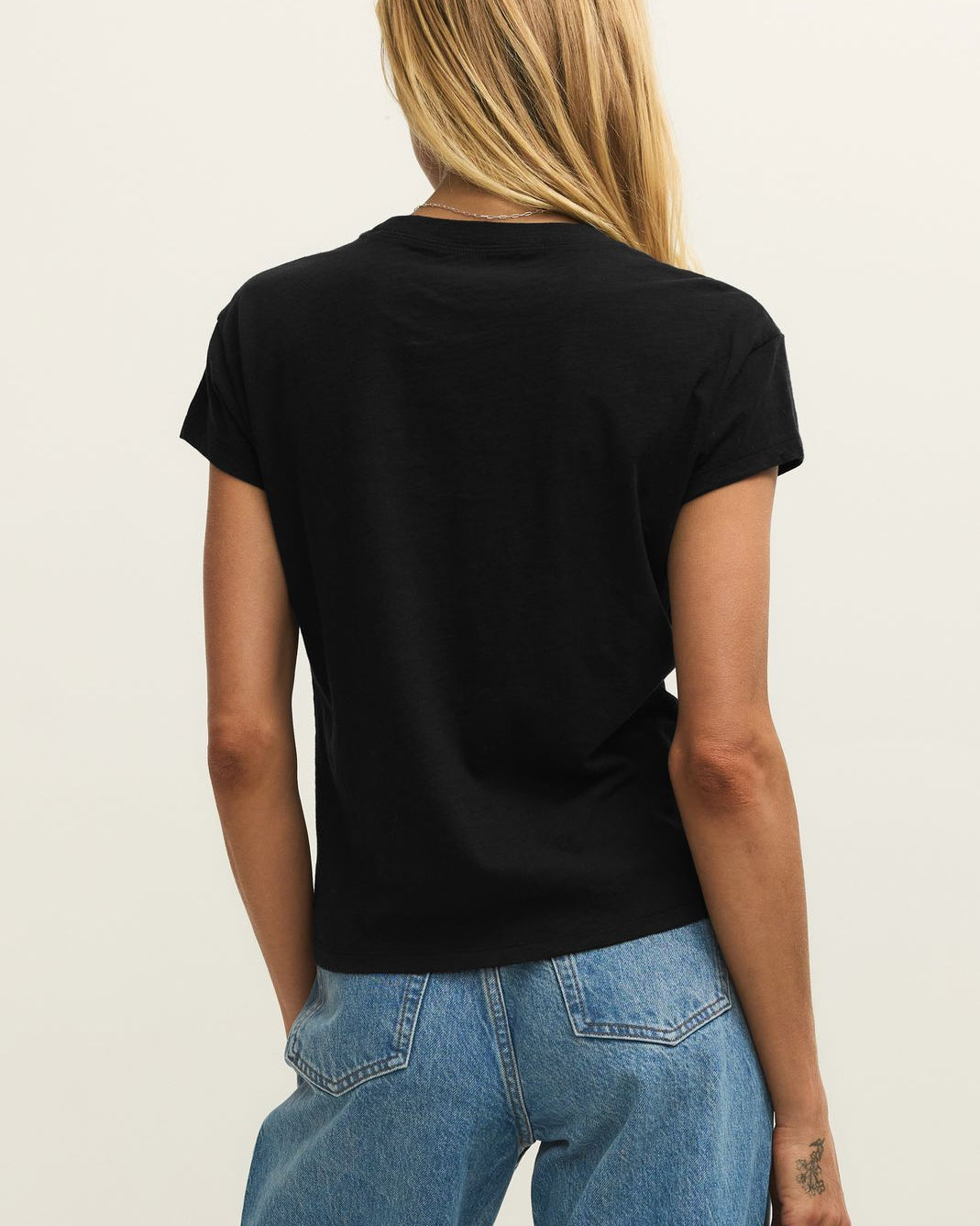 Person wearing a black t-shirt and blue jeans on a plain background