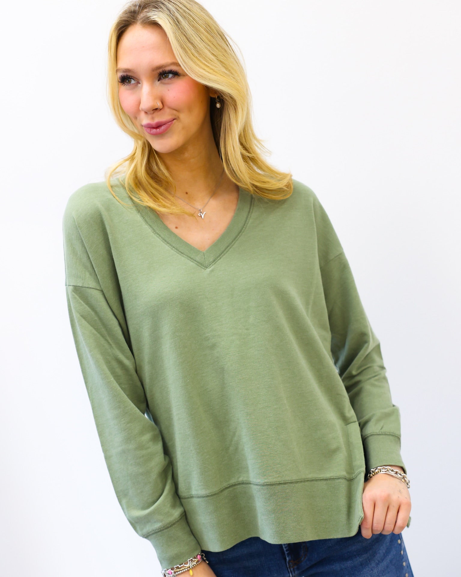 Woman wearing a green z supply sweater and blue jeans against a white background