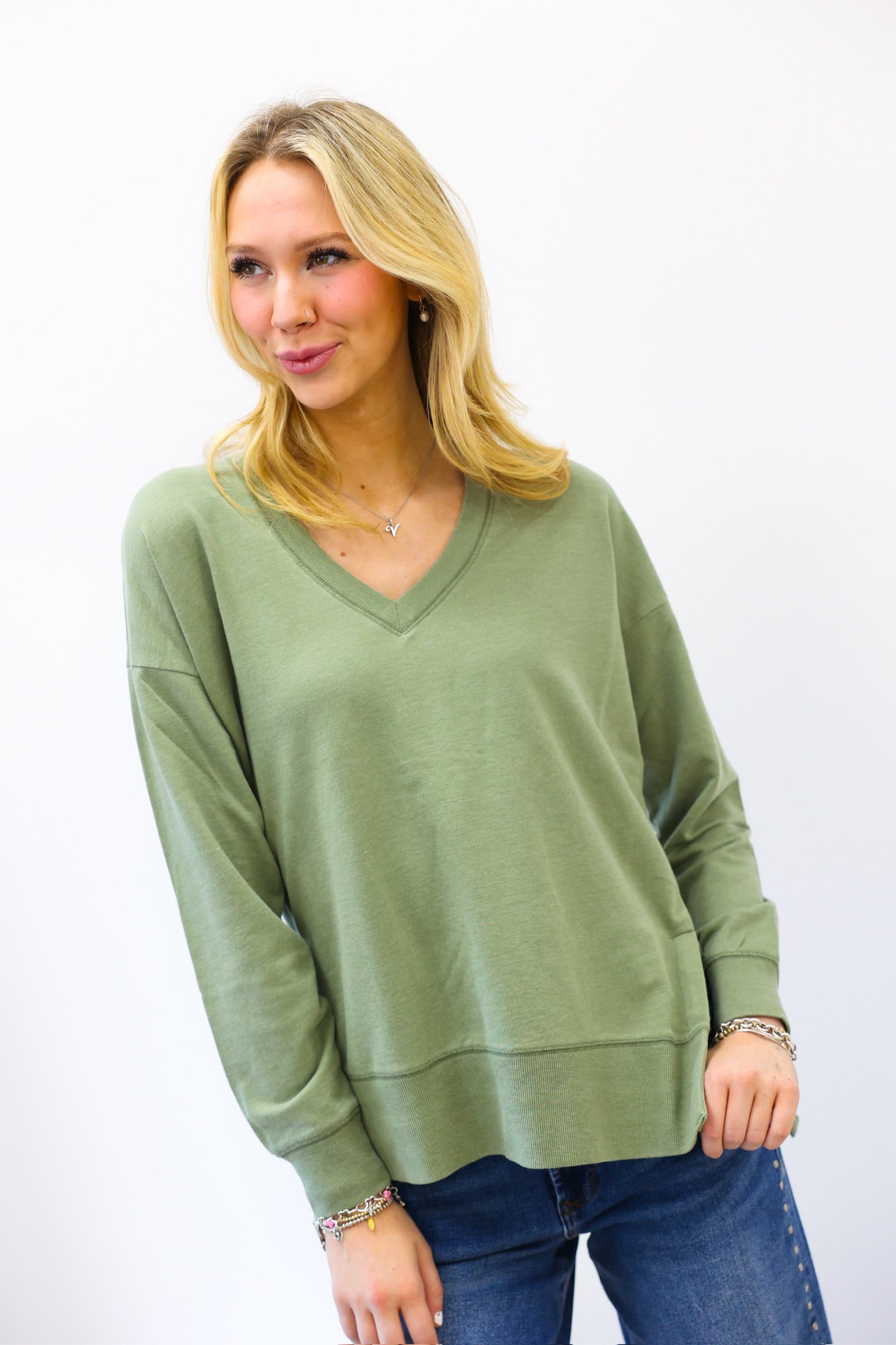 Woman wearing a green z supply sweater and blue jeans against a white background