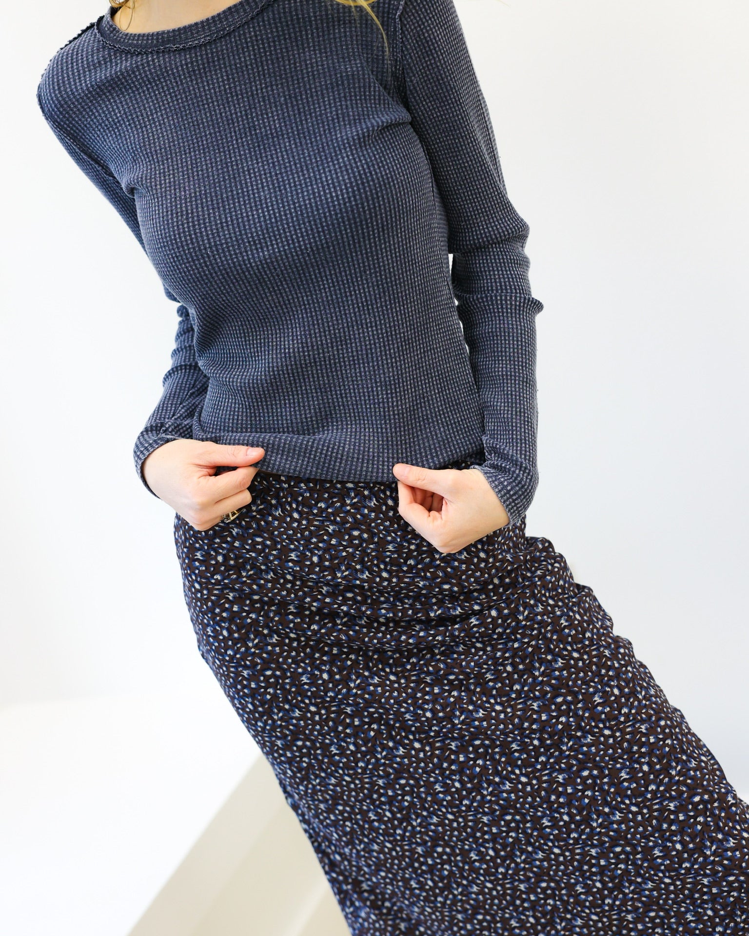 Woman wearing a blue textured sweater and patterned skirt against a white background