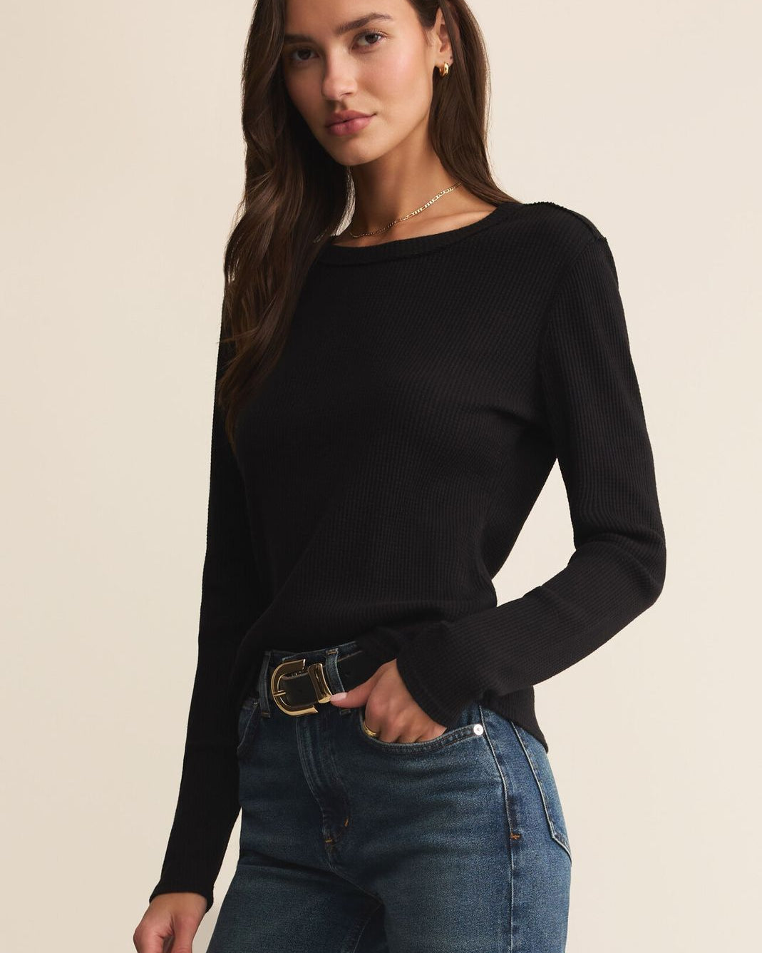 Woman wearing a black long-sleeve top and blue jeans on a beige background