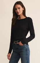 Woman wearing a black long-sleeve top and blue jeans on a beige background