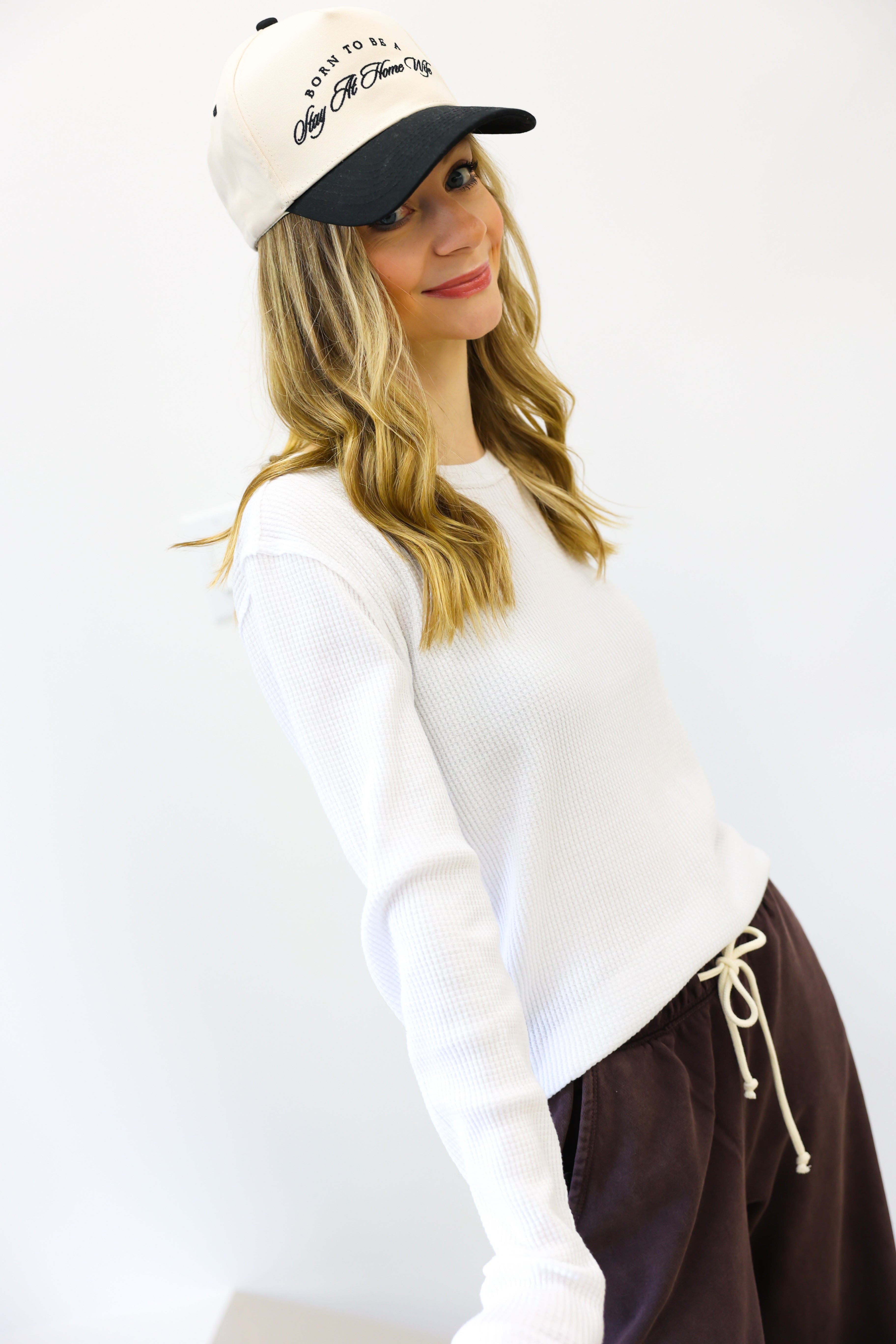Woman wearing a white sweater and brown pants with a cap on a white background
