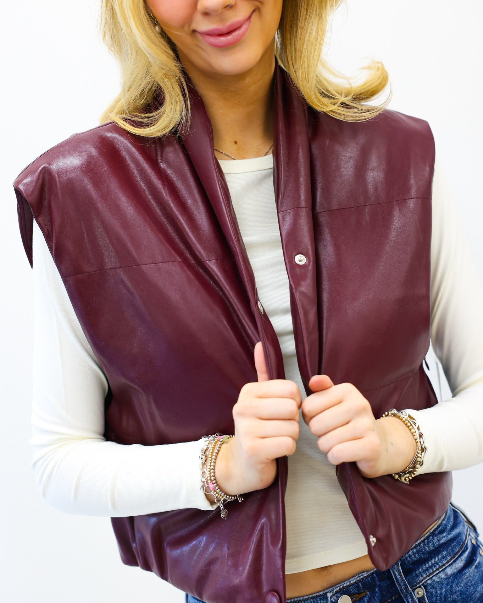 Woman wearing a maroon leather vest over a white shirt with blue jeans on a white background