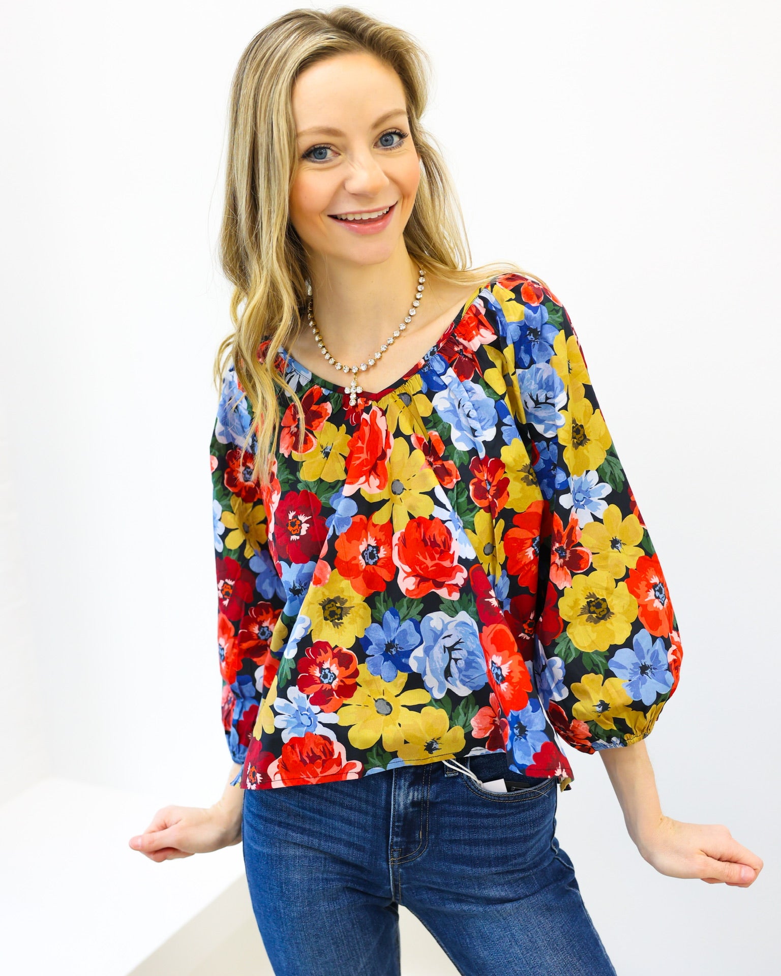 Woman wearing a colorful floral blouse and blue jeans on a white background