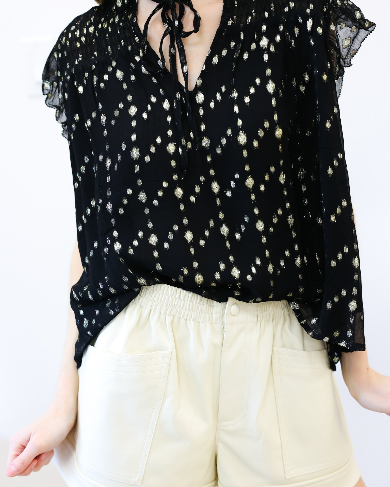 Person wearing a black floral blouse and white shorts on a white background