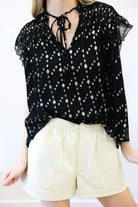 Person wearing a black floral blouse and white shorts on a white background