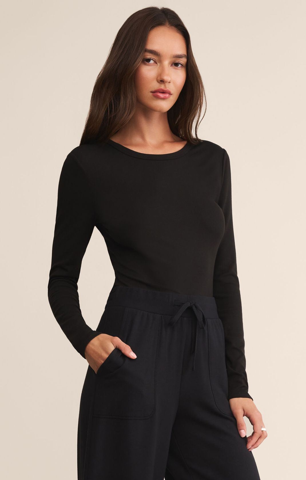 Woman wearing a black long-sleeve top and black pants on a beige background