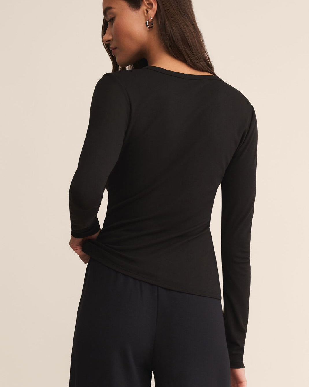 Person wearing a black long-sleeve top and pants on a beige background