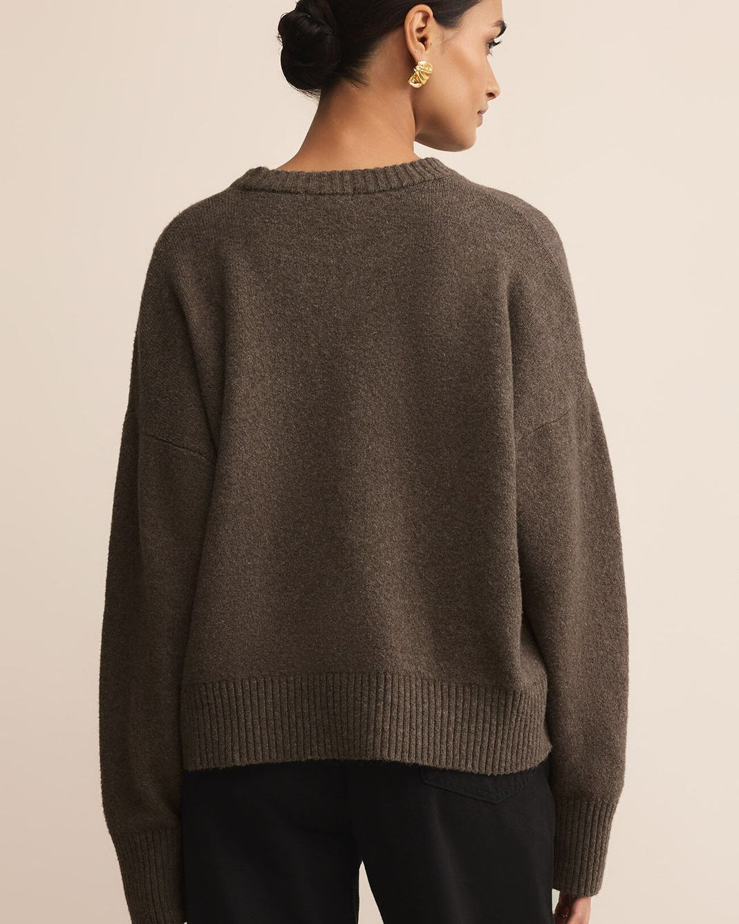 Woman wearing a brown sweater from behind on a beige background