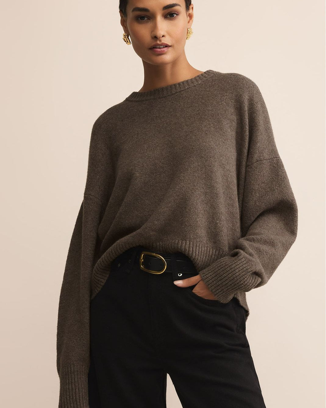 Woman wearing a brown sweater and black pants against a beige background