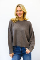 Woman wearing a brown sweater and blue jeans against a white background