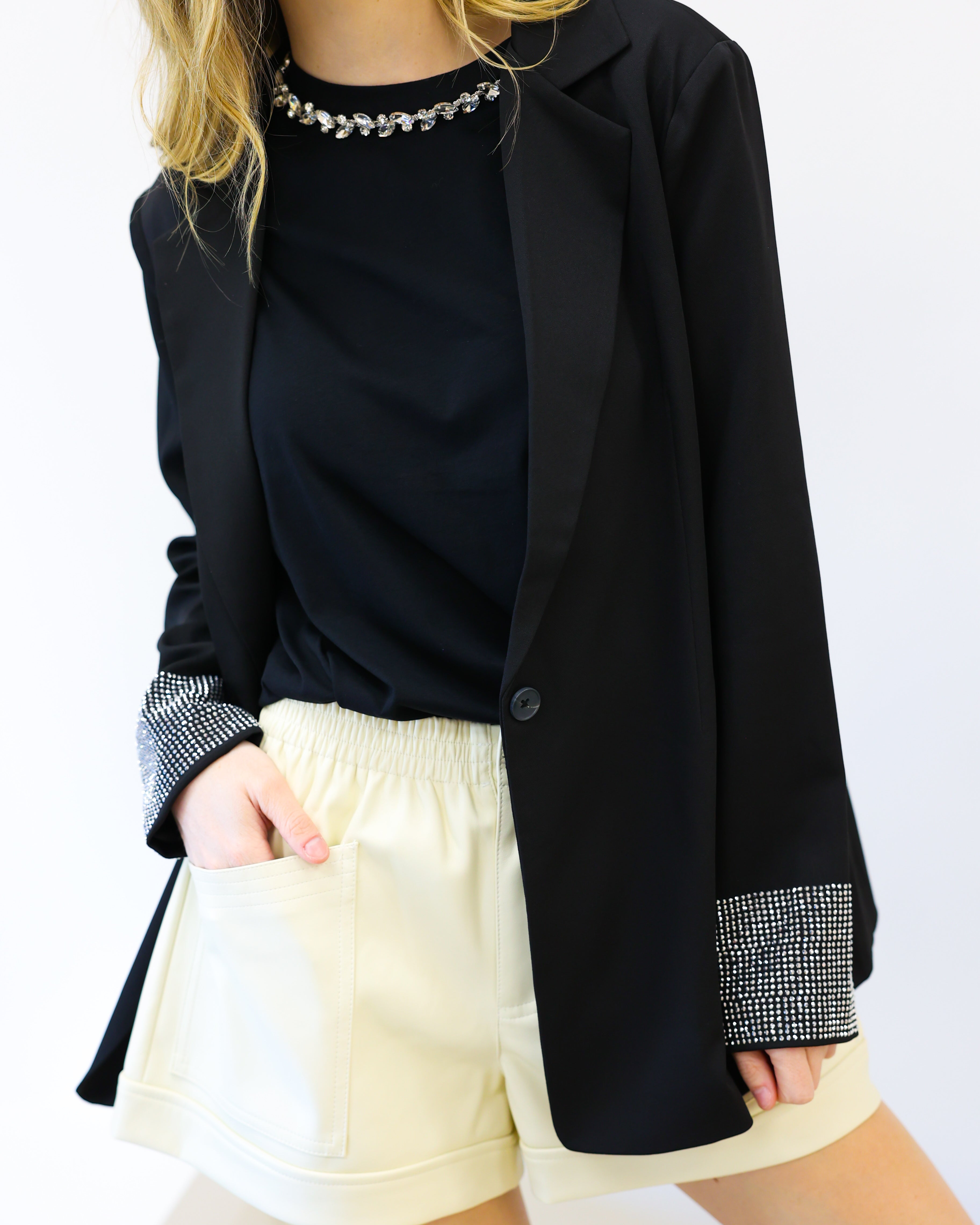 Person wearing a black blazer, black top, and white shorts on a white background