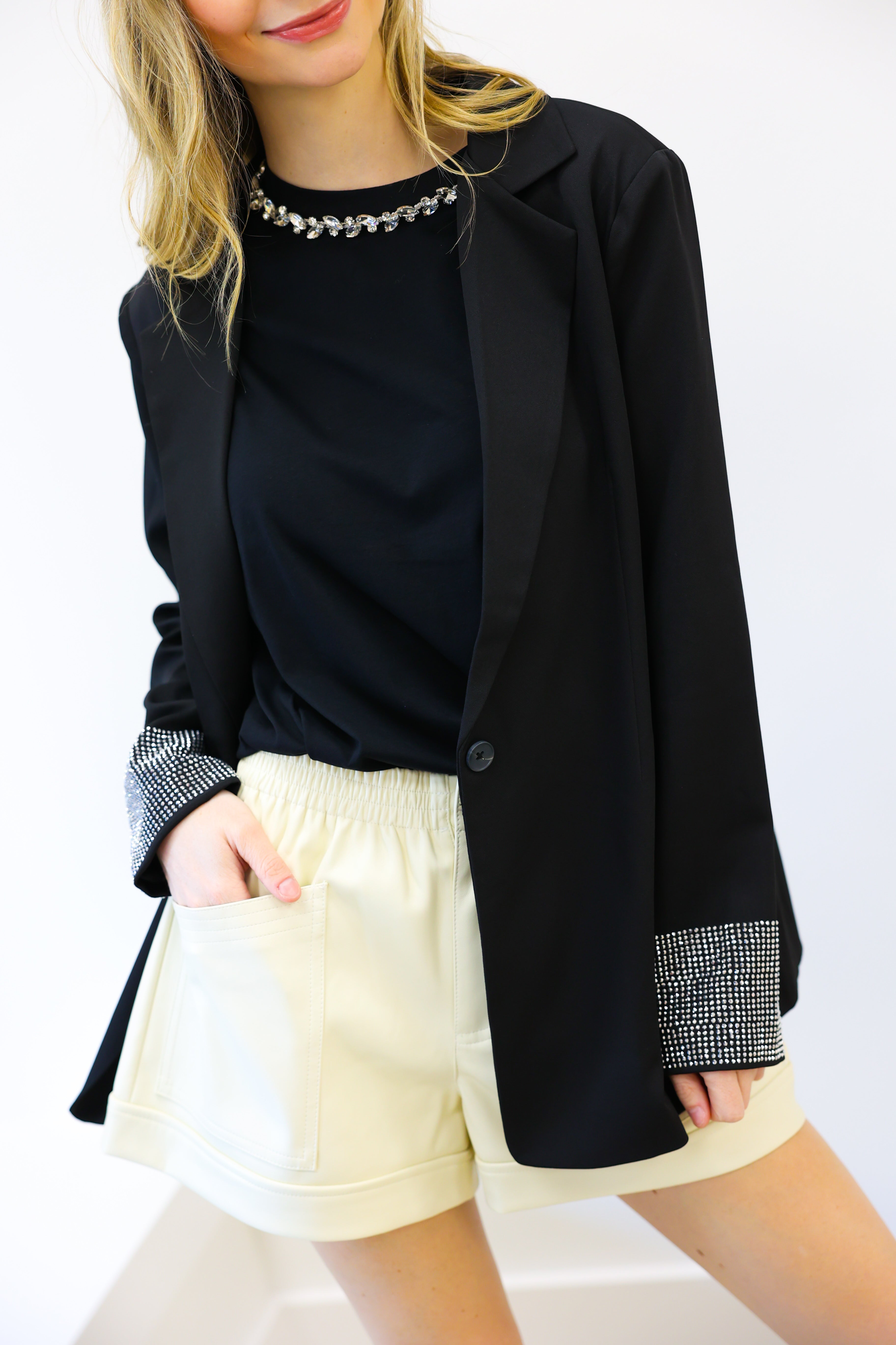 Person wearing a black blazer, black top, and white shorts on a white background