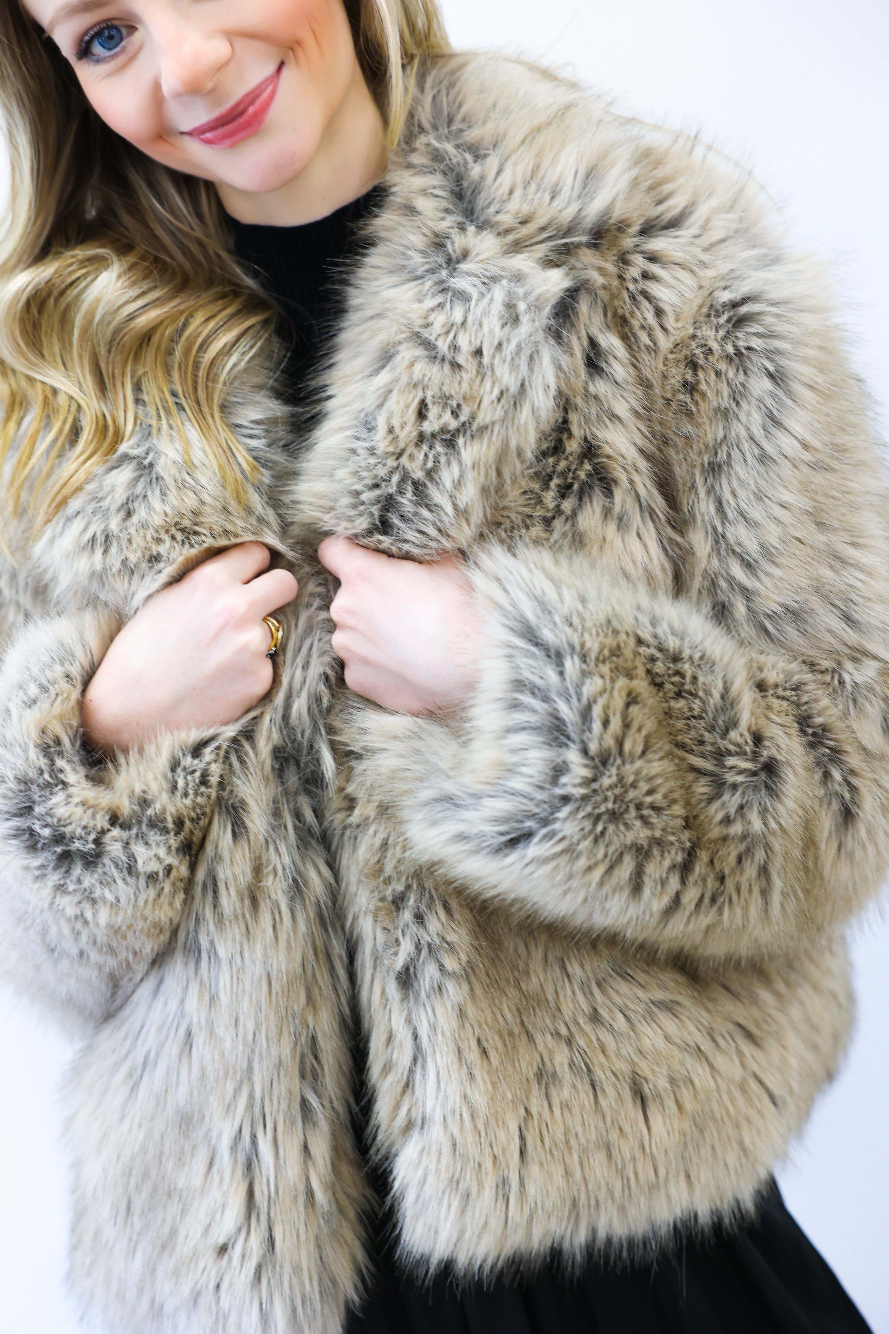 Person wearing a fluffy beige coat against a white background