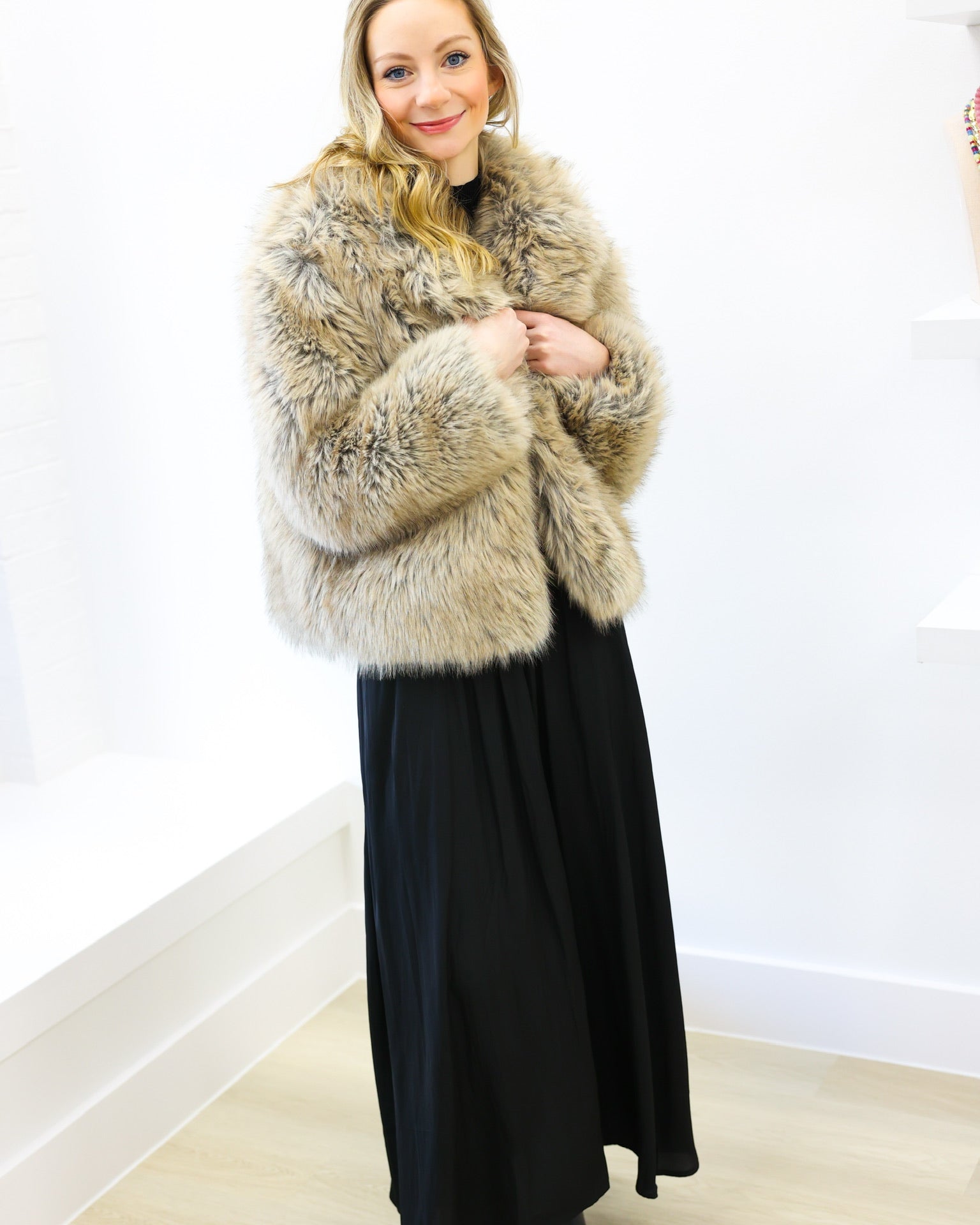 Woman wearing a fur coat and black dress against a white wall
