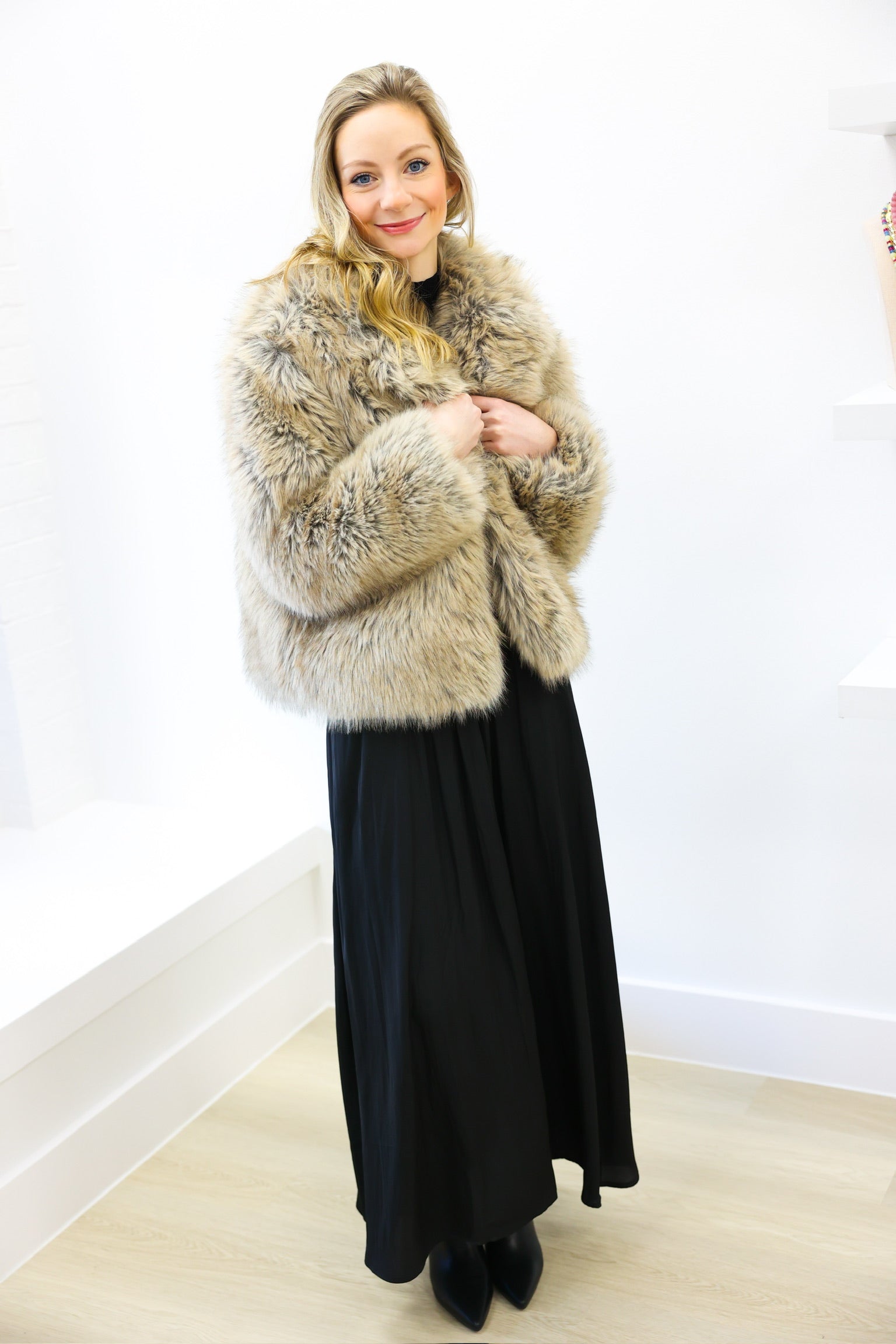 Woman wearing a fur coat and black dress against a white wall