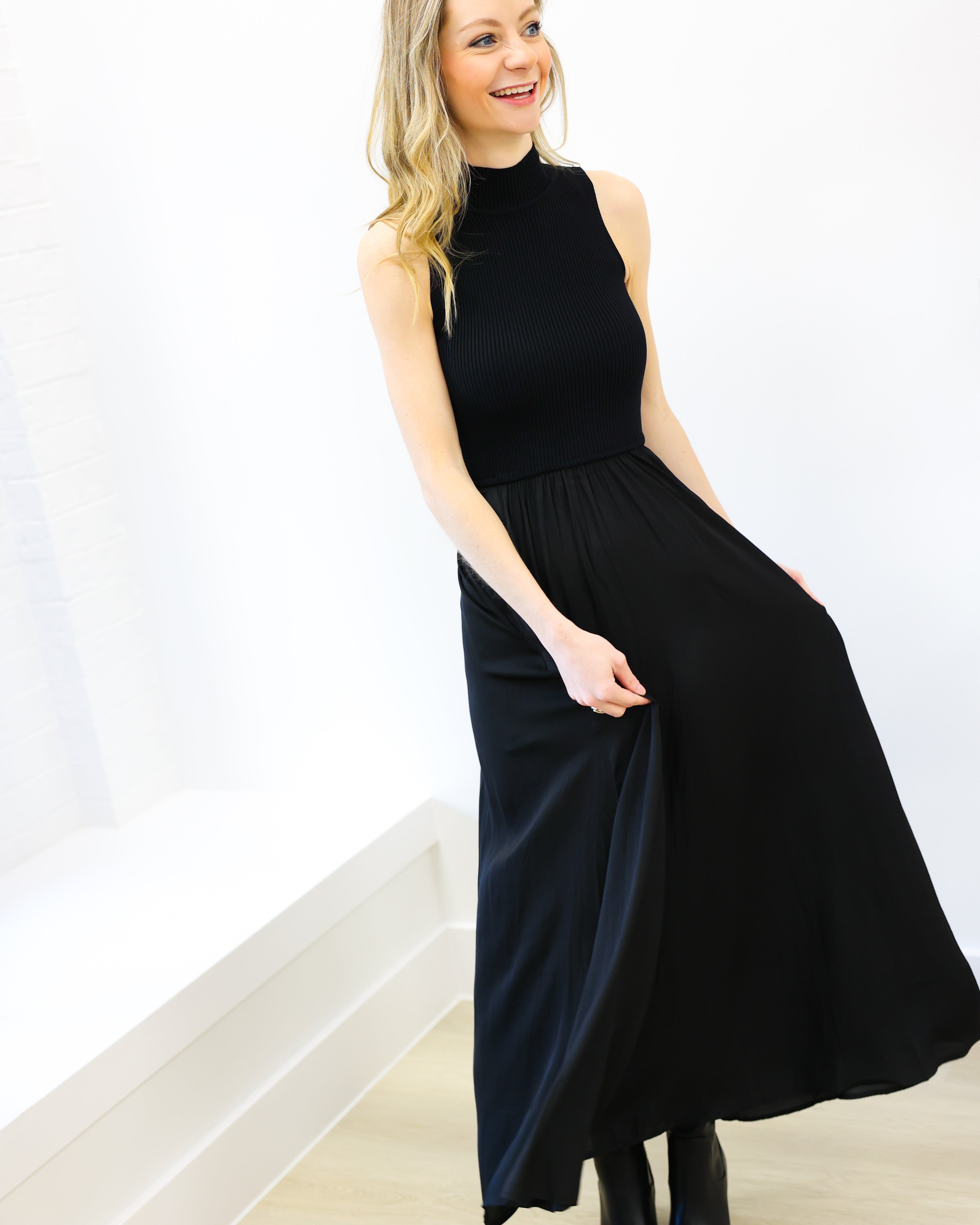 Woman wearing a black sleeveless dress against a white wall.