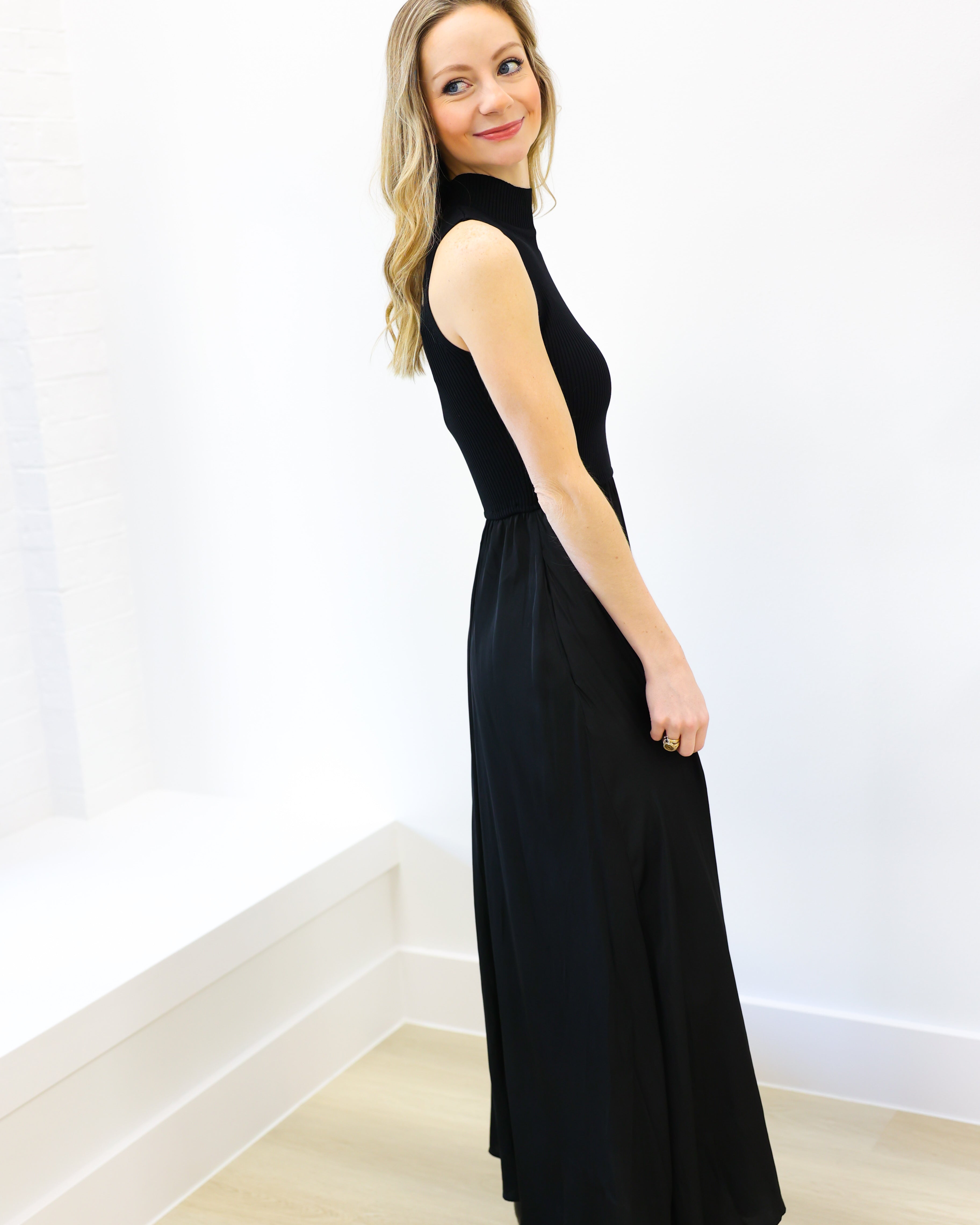 Woman wearing a black sleeveless dress against a white wall.