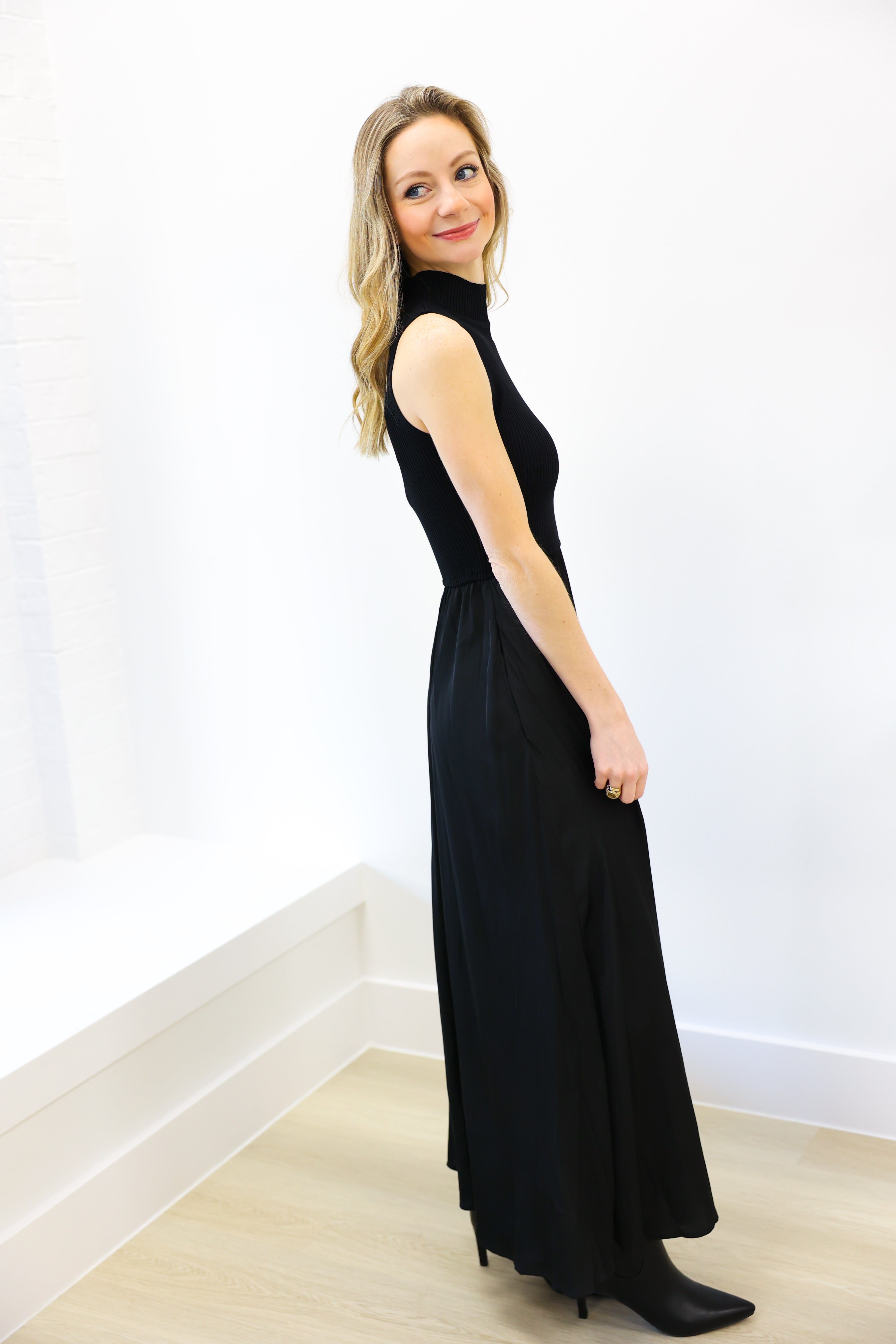 Woman wearing a black sleeveless dress against a white wall.