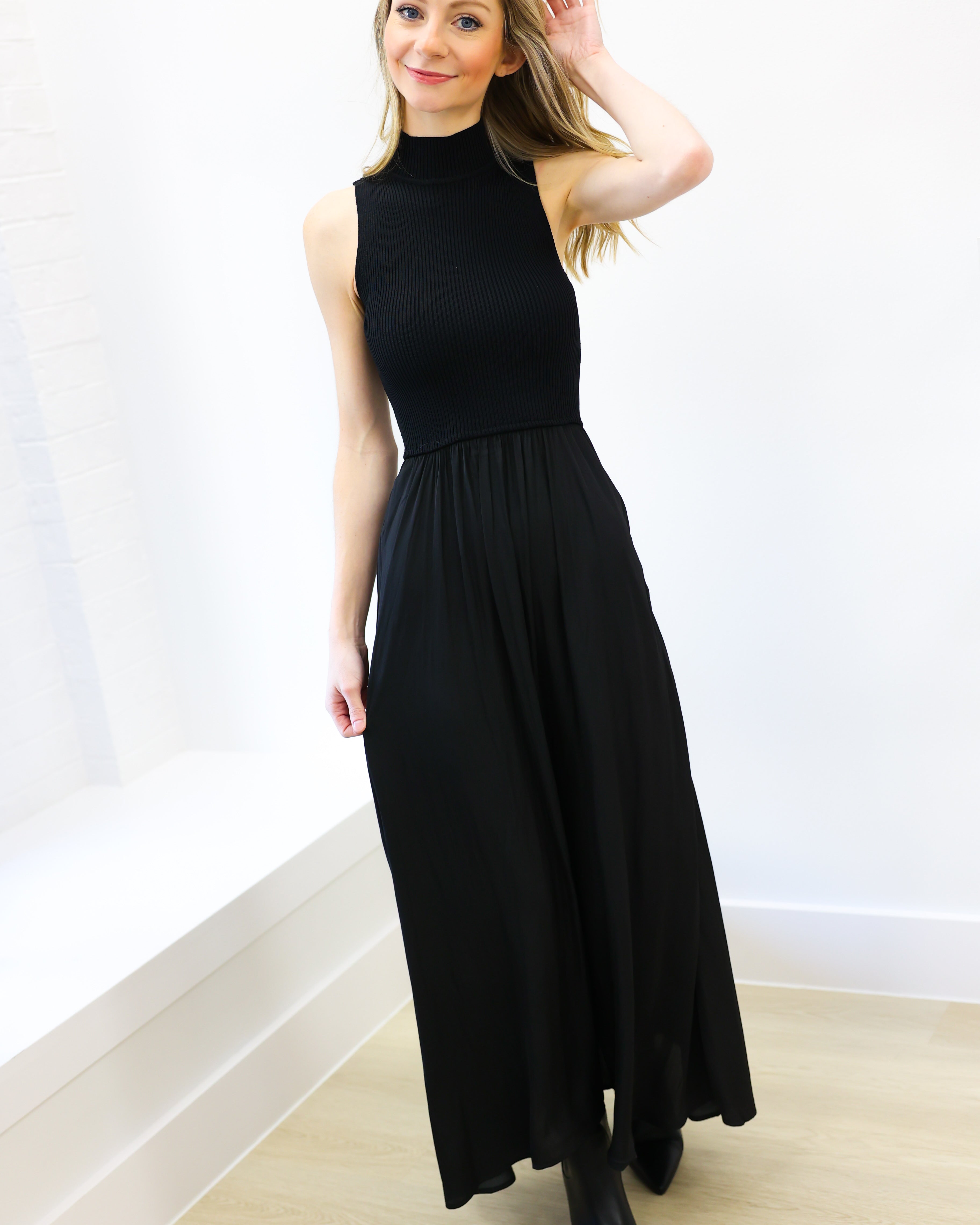 Woman wearing a black sleeveless dress against a white wall.