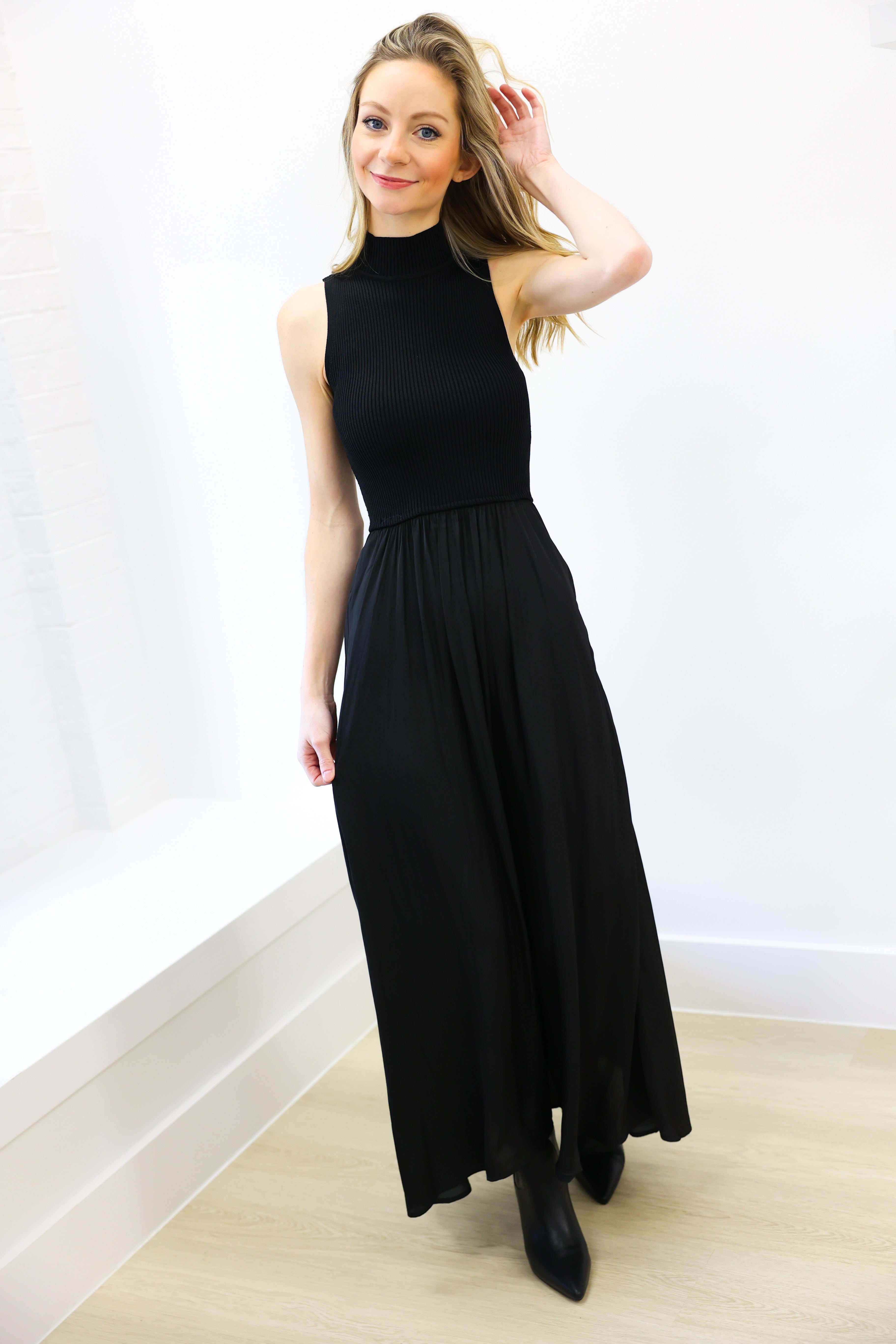 Woman wearing a black sleeveless dress against a white wall.