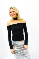 Woman wearing a black off-shoulder top and silver sequin skirt on a white background