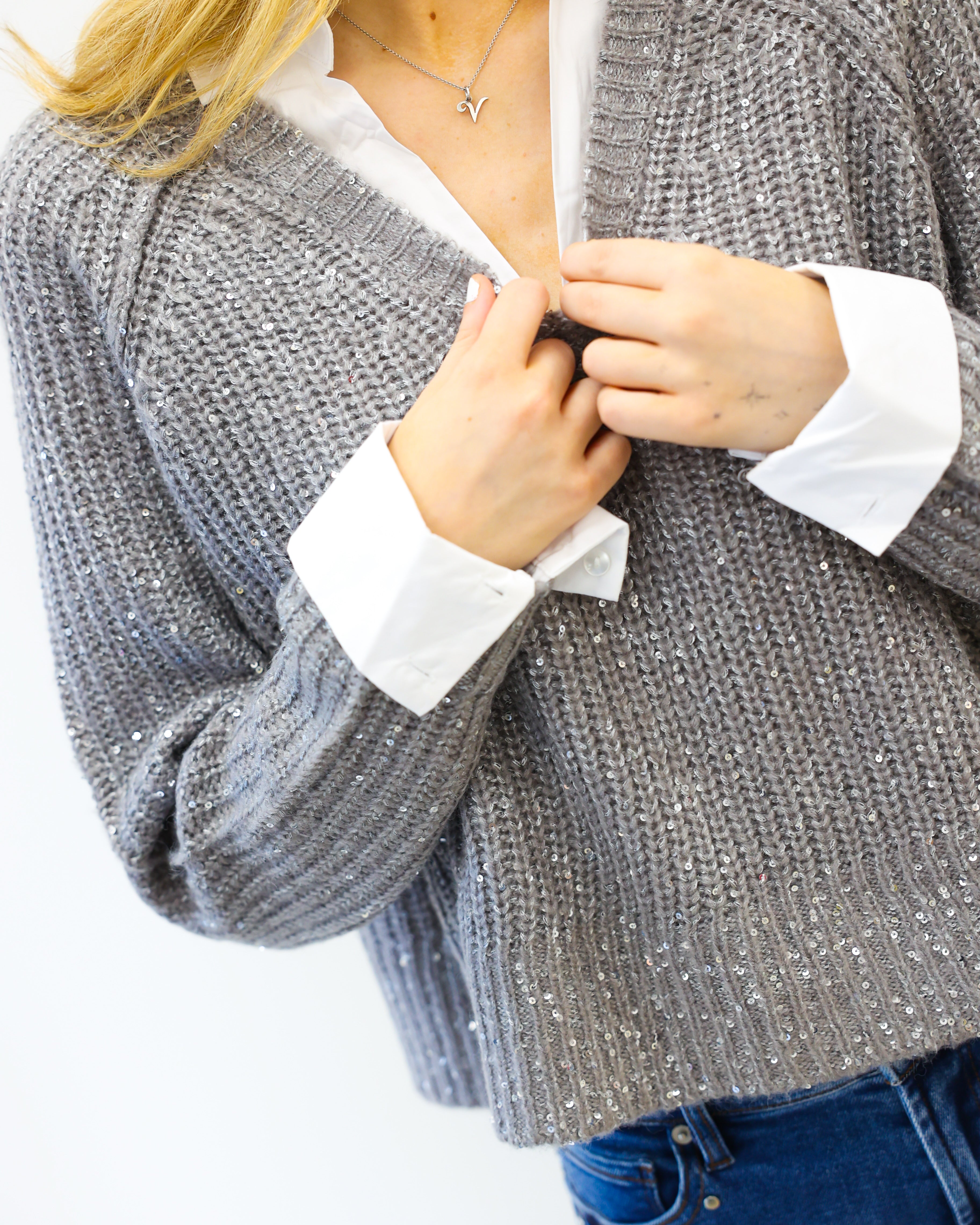 Person wearing a gray knitted cardigan over a white shirt with blue jeans on a white background