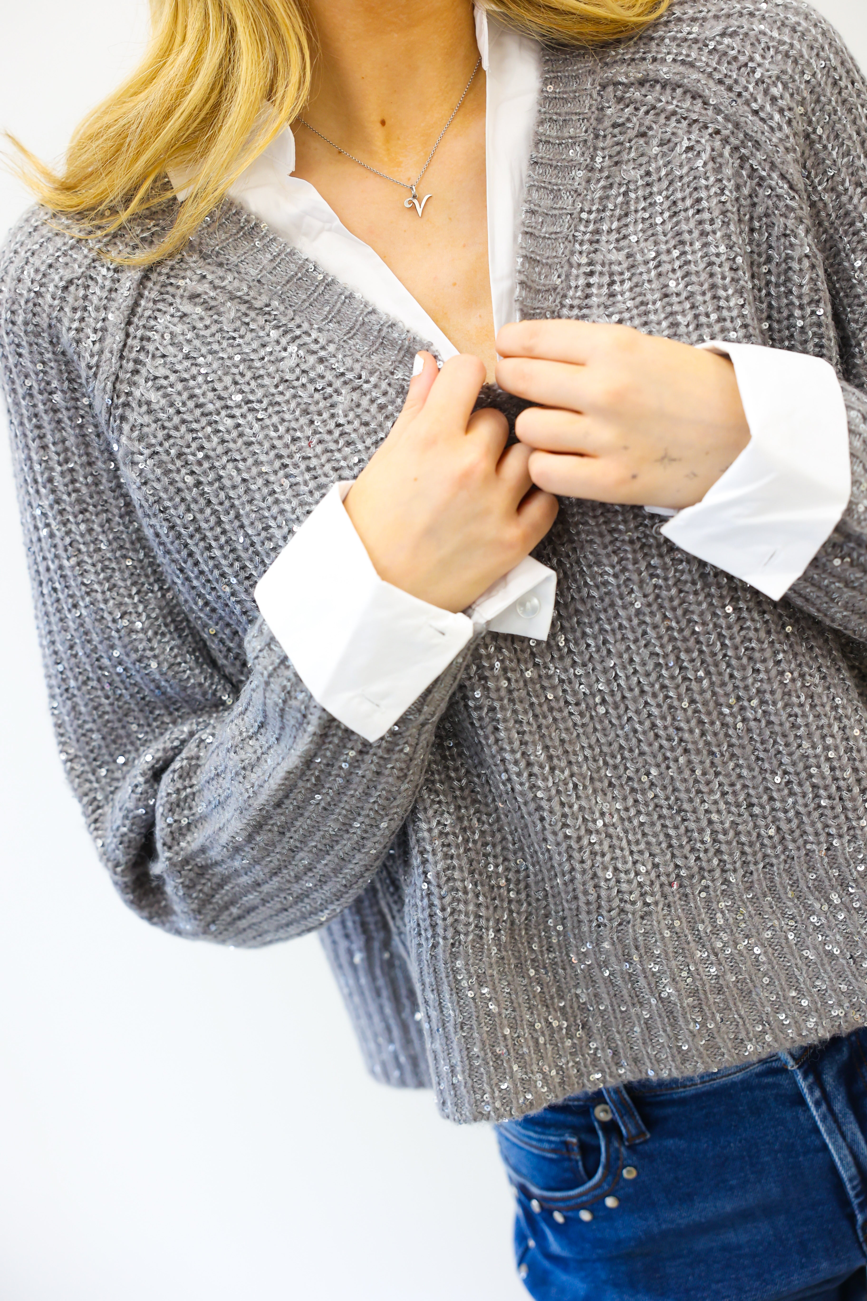 Person wearing a gray knitted cardigan over a white shirt with blue jeans on a white background