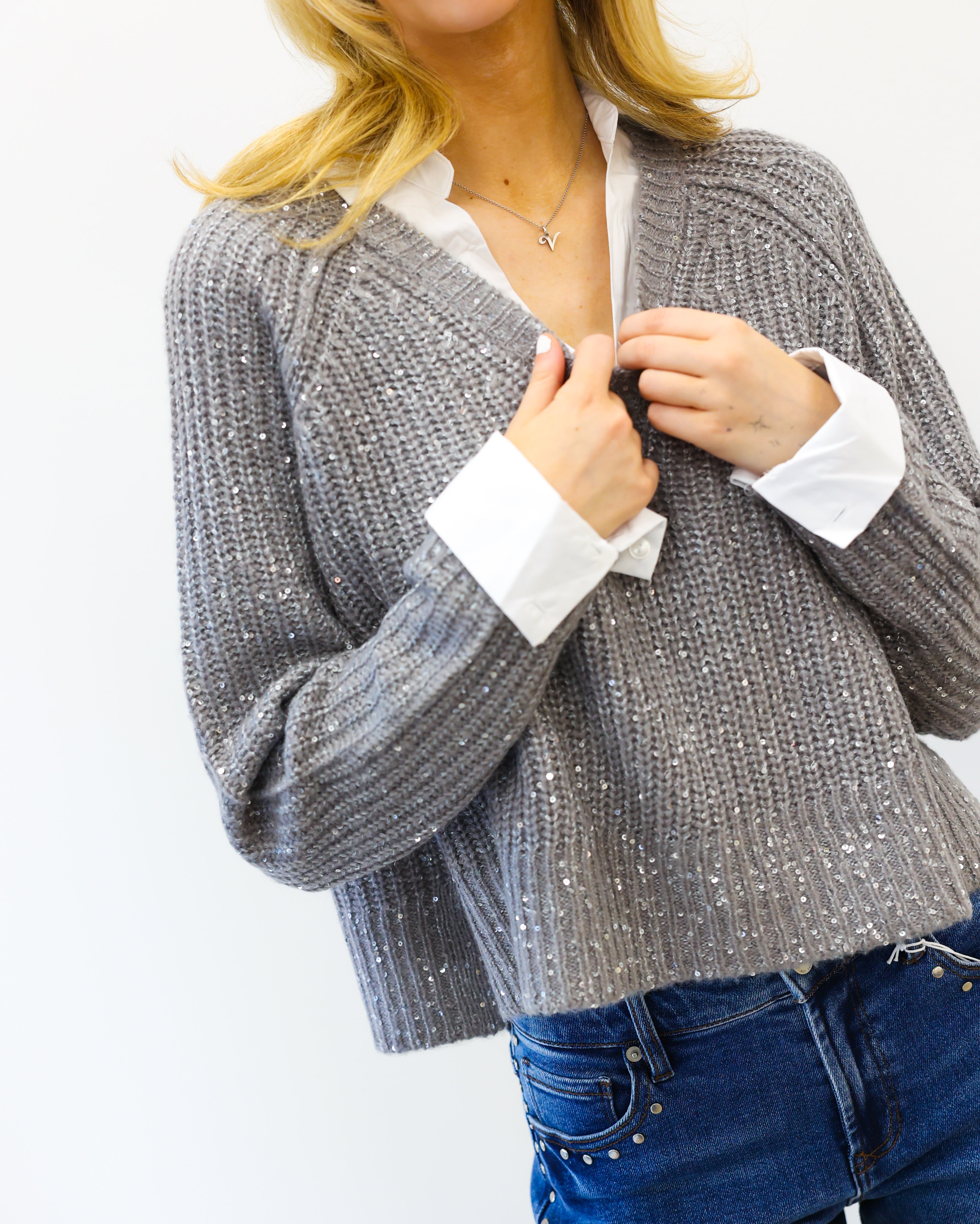 Woman wearing a gray knitted cardigan over a white shirt with blue jeans on a white background
