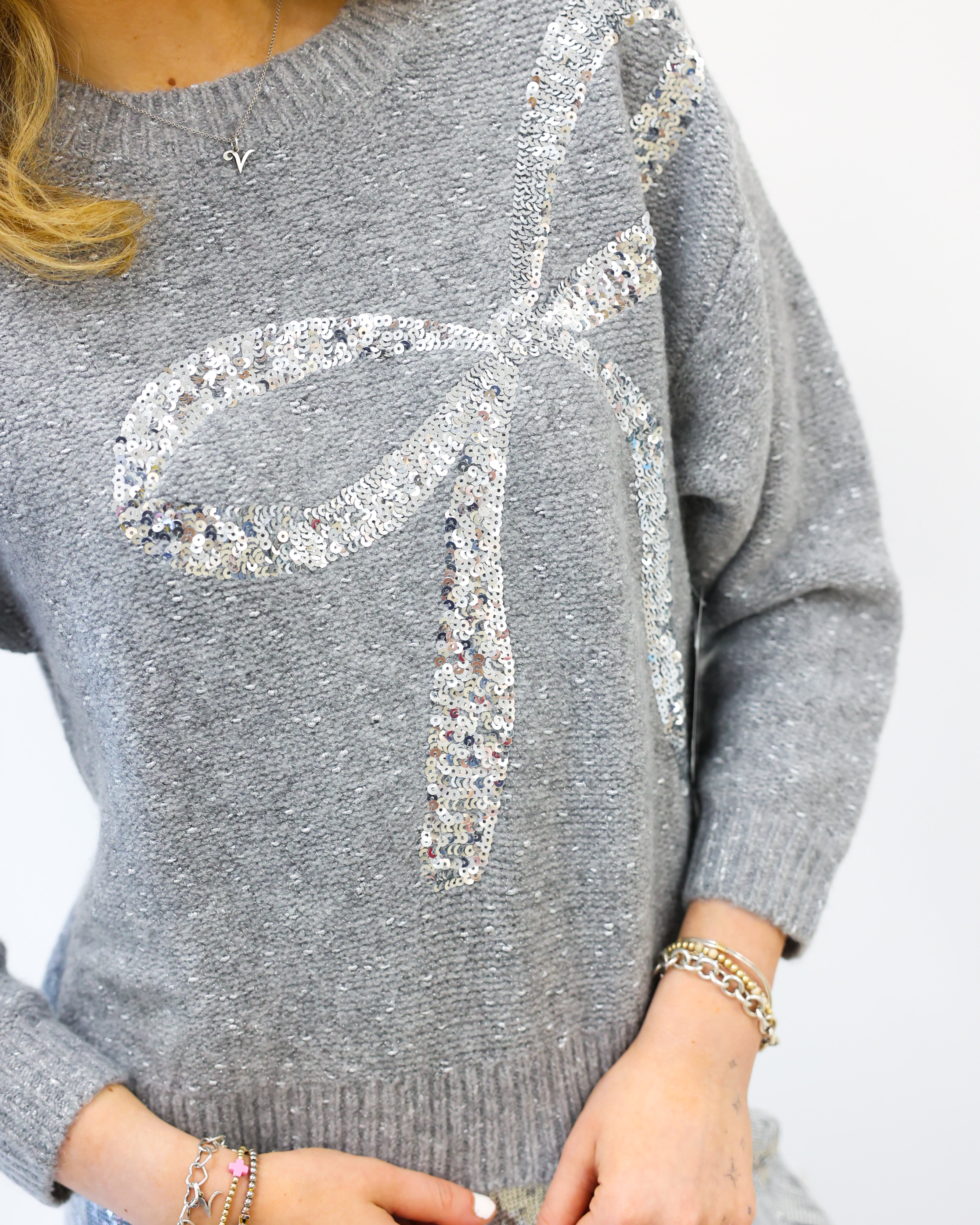 Gray sweater with a decorative bow design on a plain background