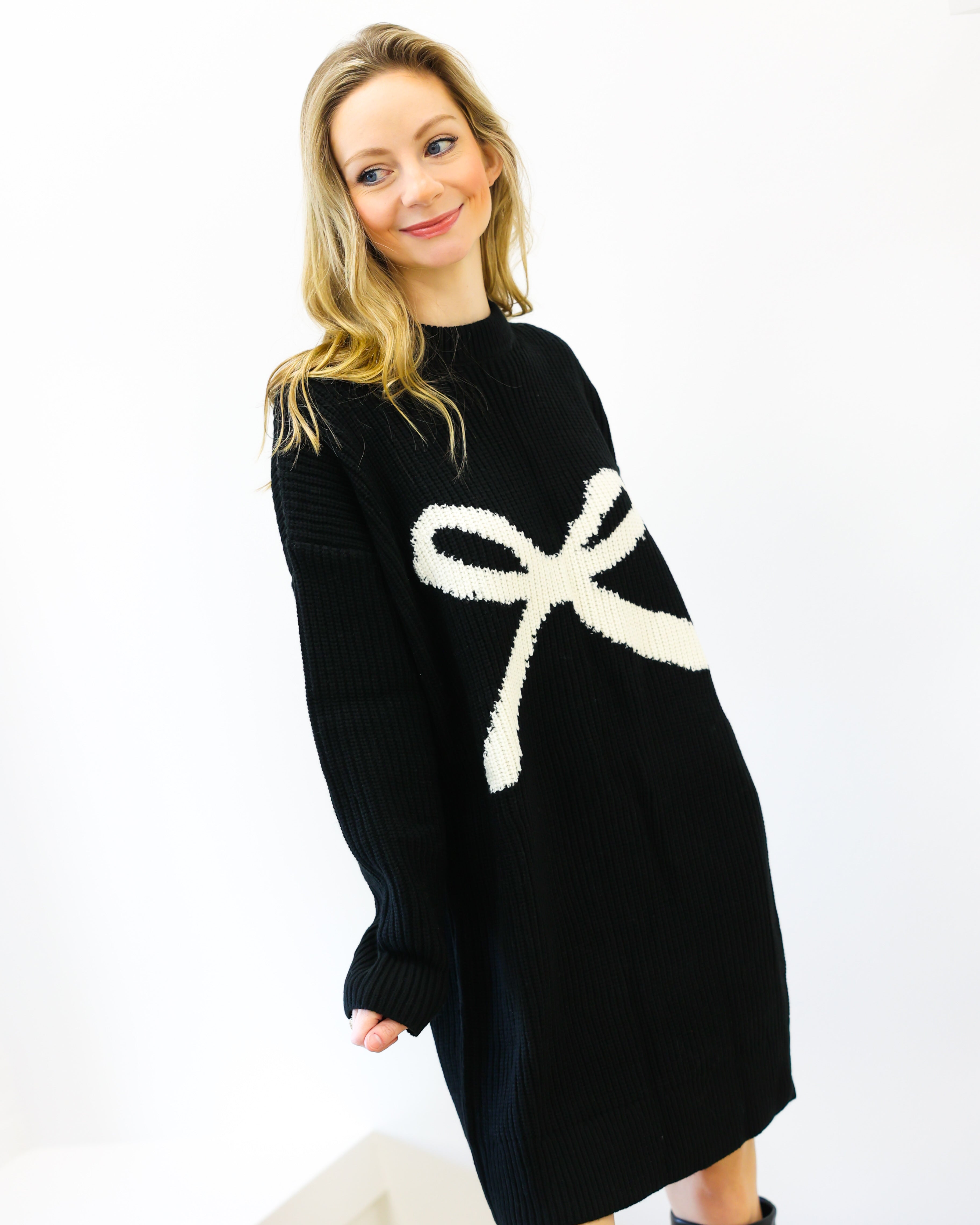 Woman wearing a black sweater dress with a white bow design on a white background