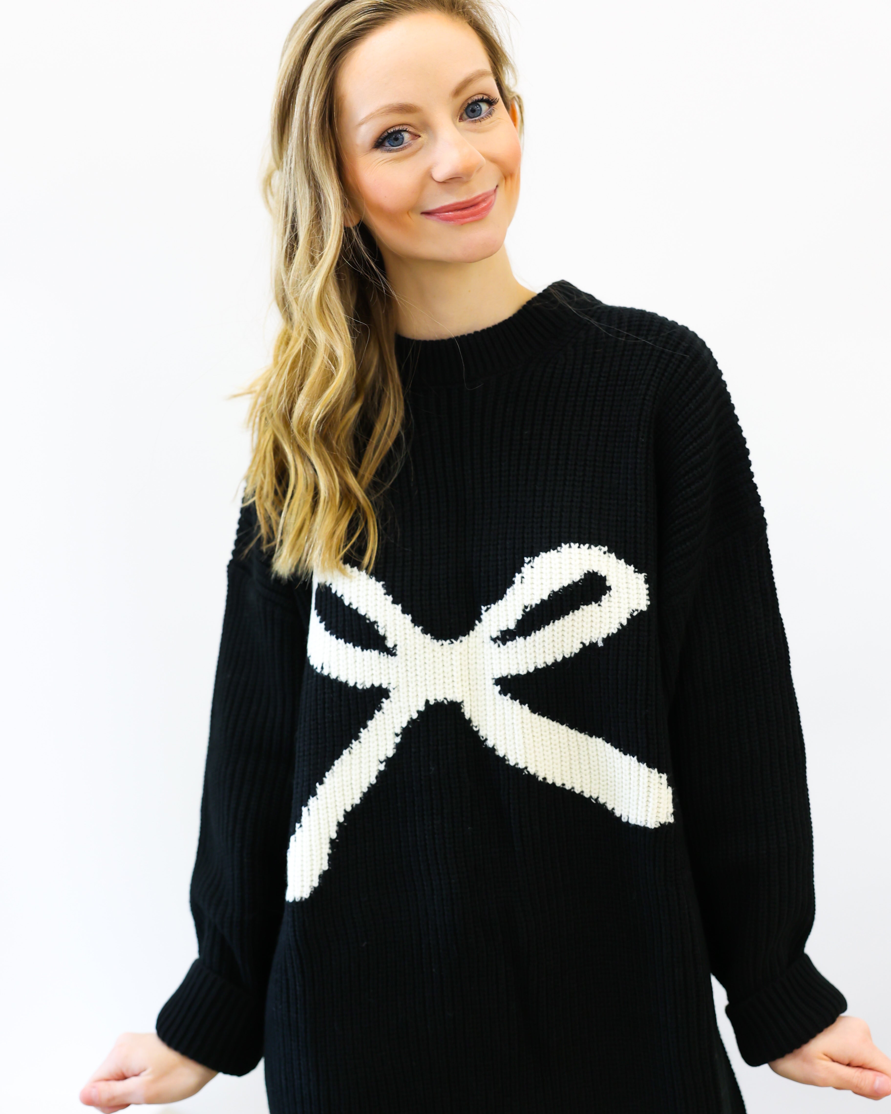 Woman wearing a black sweater with a white bow design on a white background