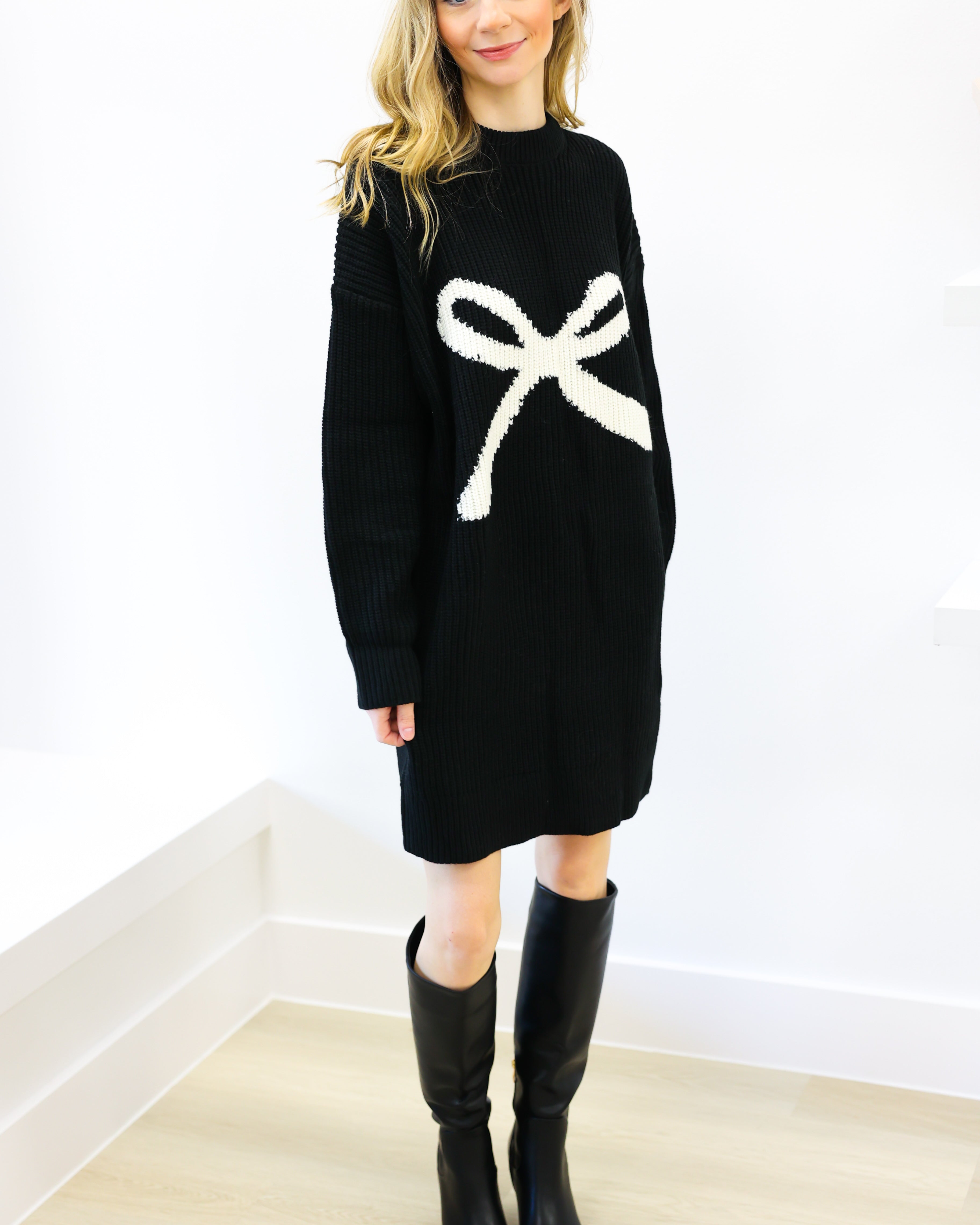 Woman wearing a black sweater dress with a white bow design against a white background