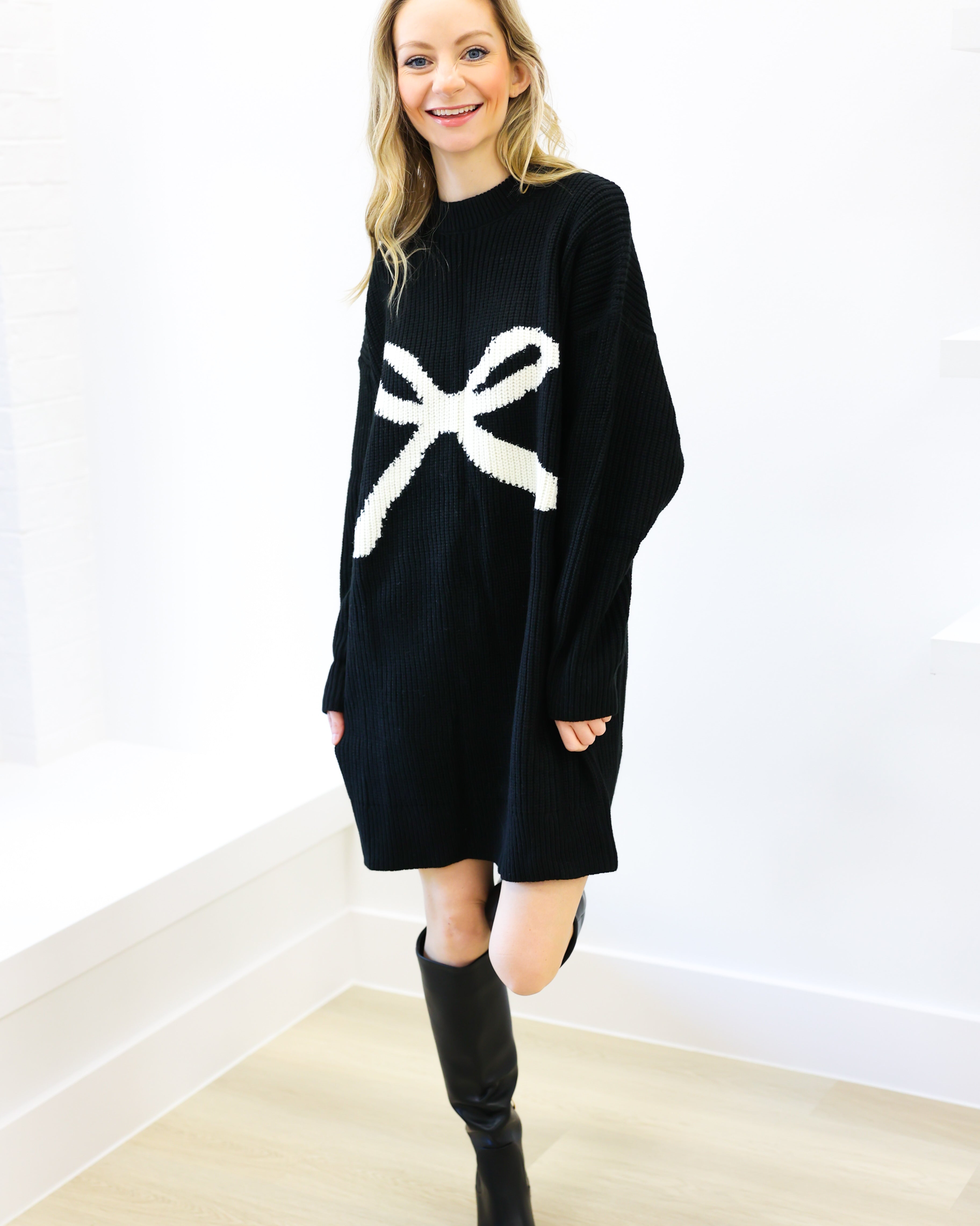 Woman wearing a black sweater dress with a white bow design on a white background
