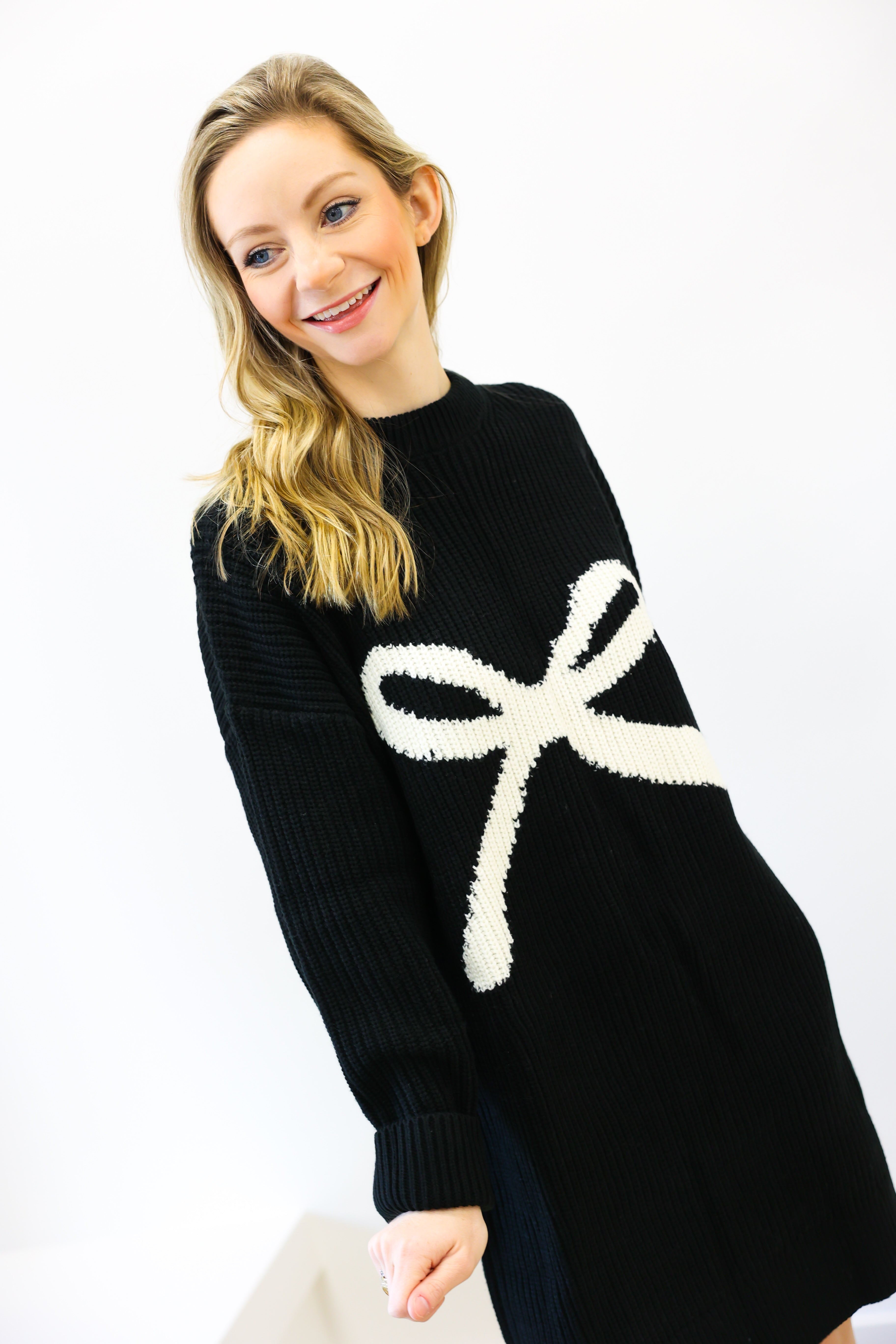 Woman wearing a black sweater with a white bow design on a white background