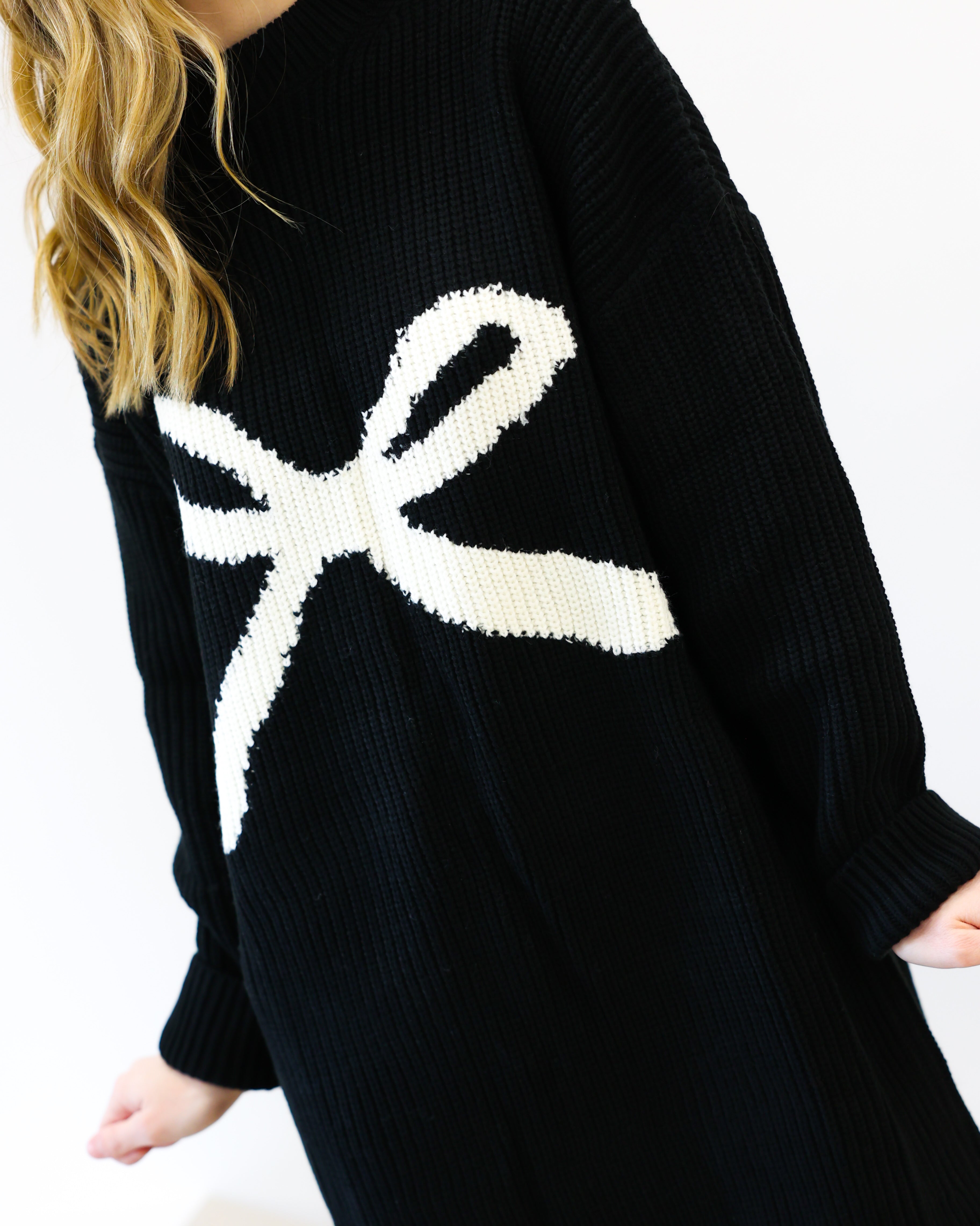 Black sweater with a white bow design worn by a person on a white background