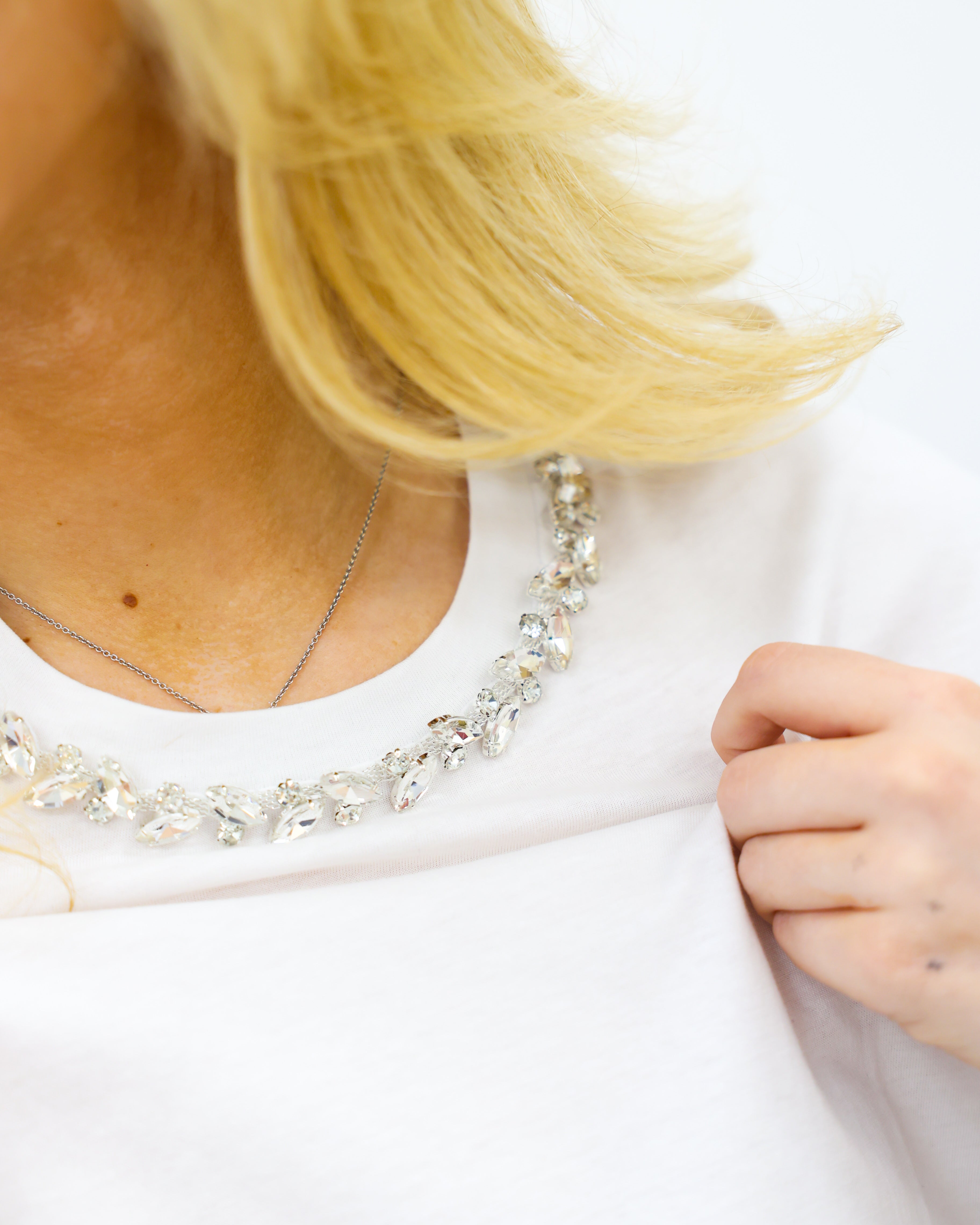 Close-up of a person wearing a white shirt with a necklace, focusing on the neckline.