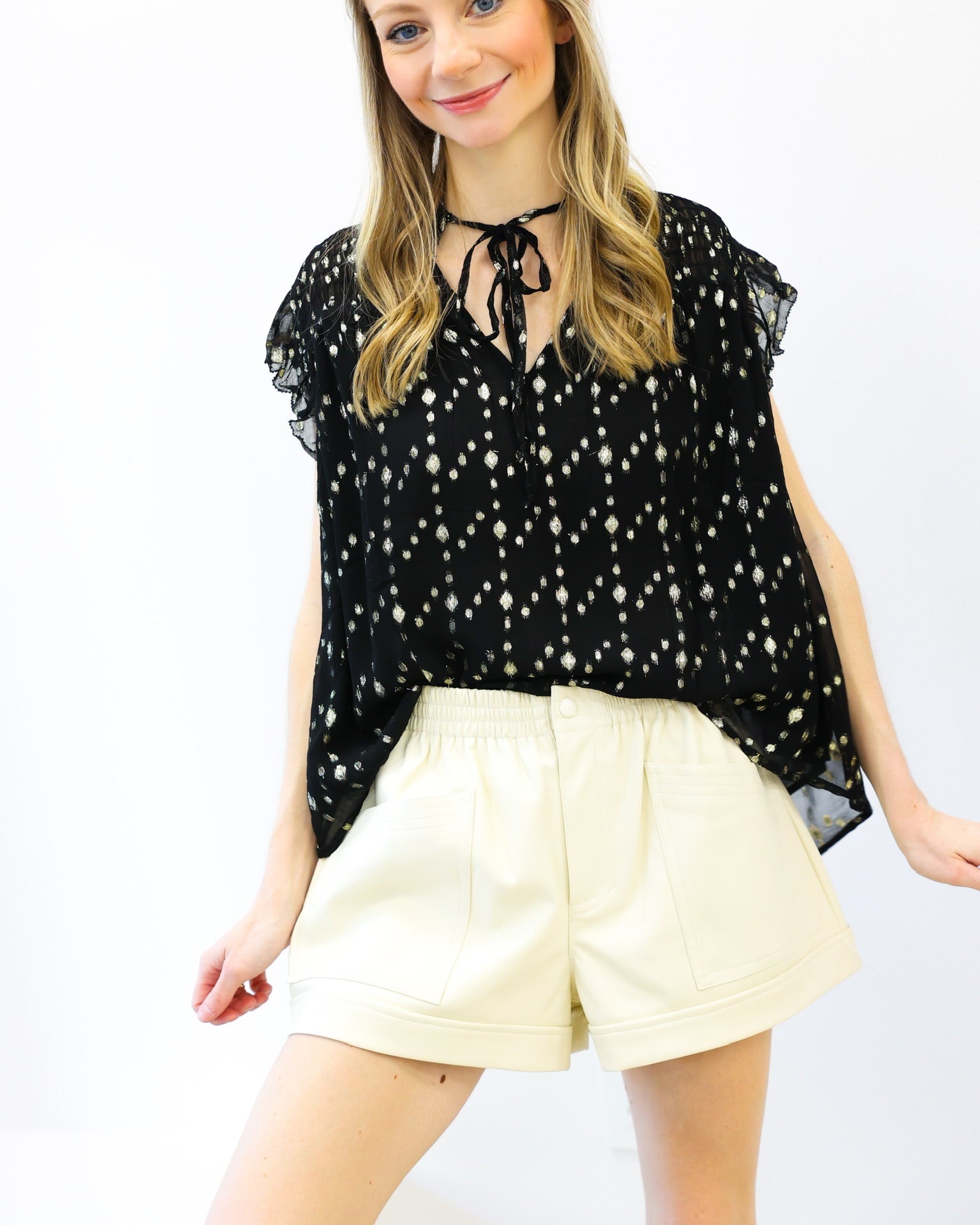 Woman wearing a black floral blouse and cream shorts on a white background