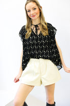 Woman wearing a black floral blouse and cream shorts on a white background