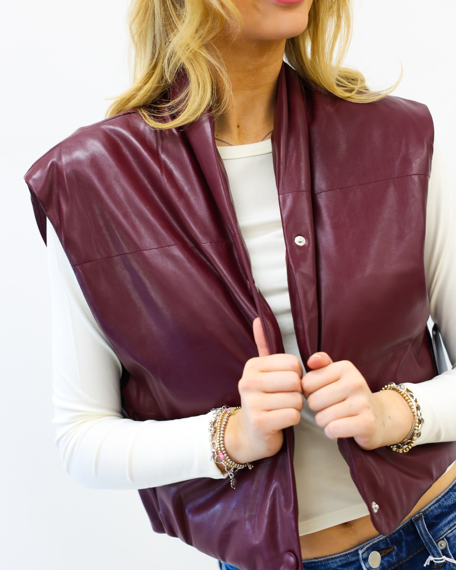 Woman wearing a burgundy leather vest over a white shirt with a plain background