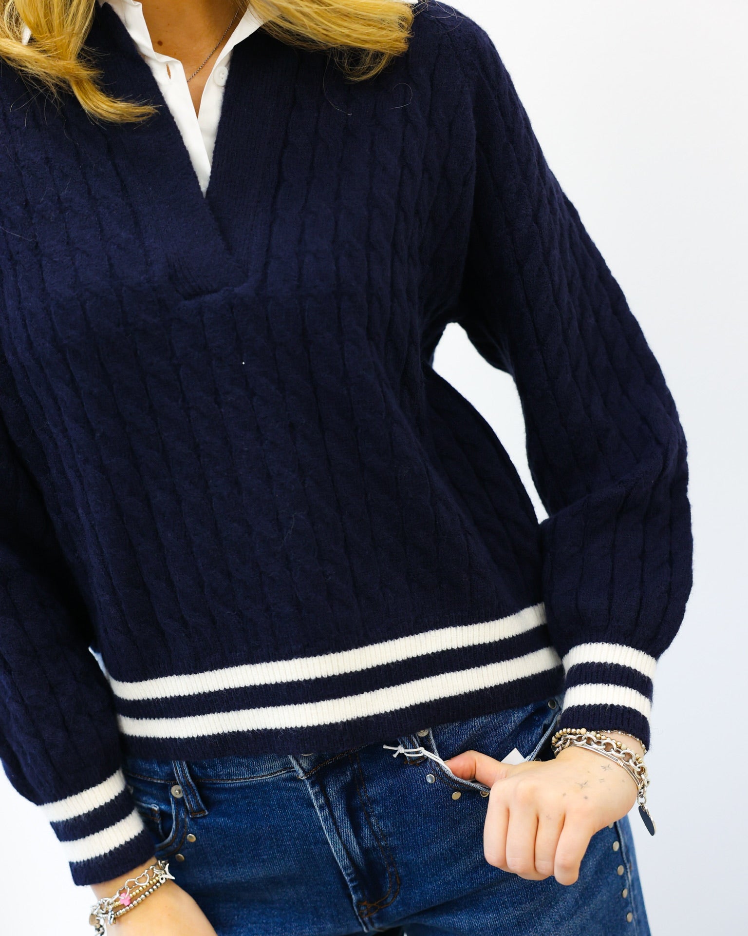 Navy sweater with white stripes worn by a person on a plain background