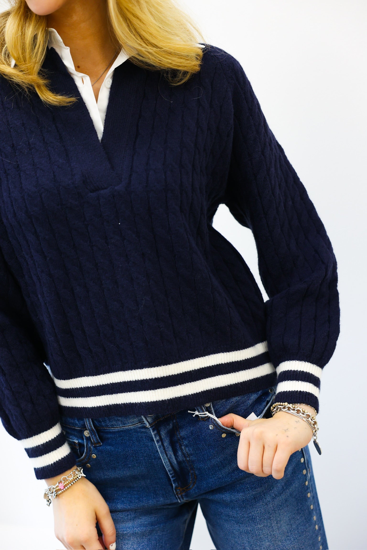 Navy sweater with white stripes worn by a person on a plain background
