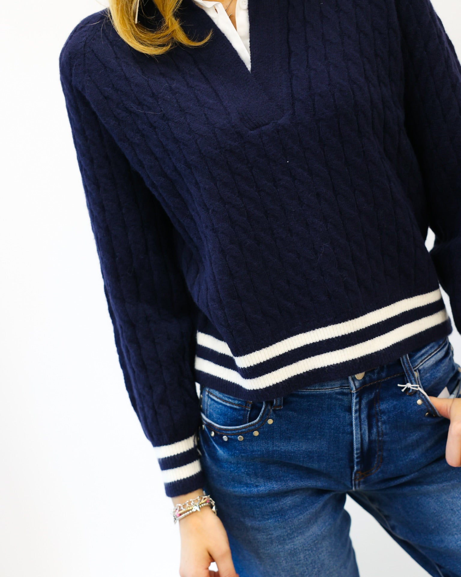 Person wearing a navy sweater with white trim and blue jeans on a white background
