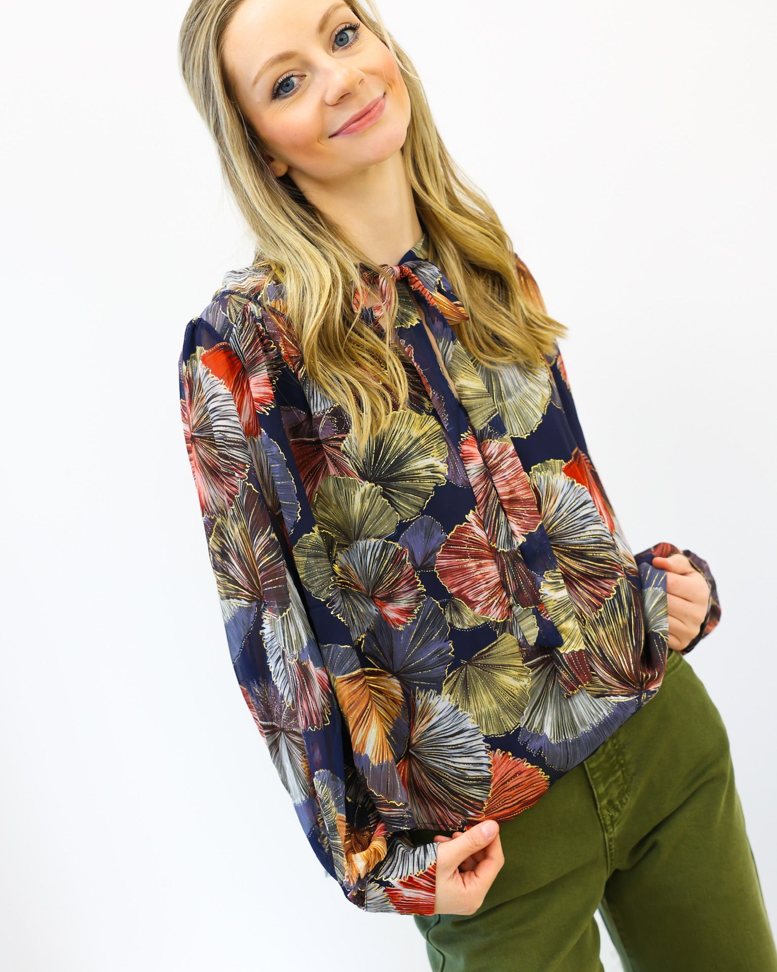 Woman wearing a colorful patterned shirt and green pants on a white background